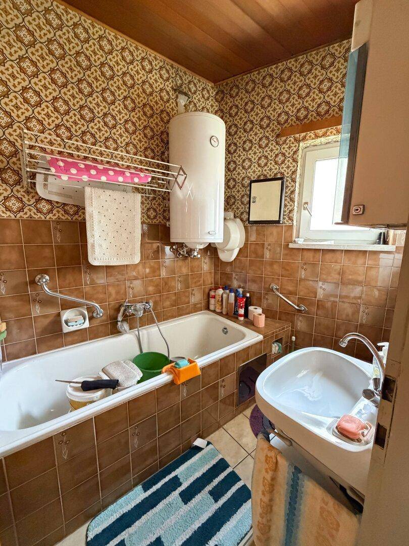 Badezimmer mit Badewanne, Waschbecken und braunen Fliesen im 80er-Jahre-Stil.