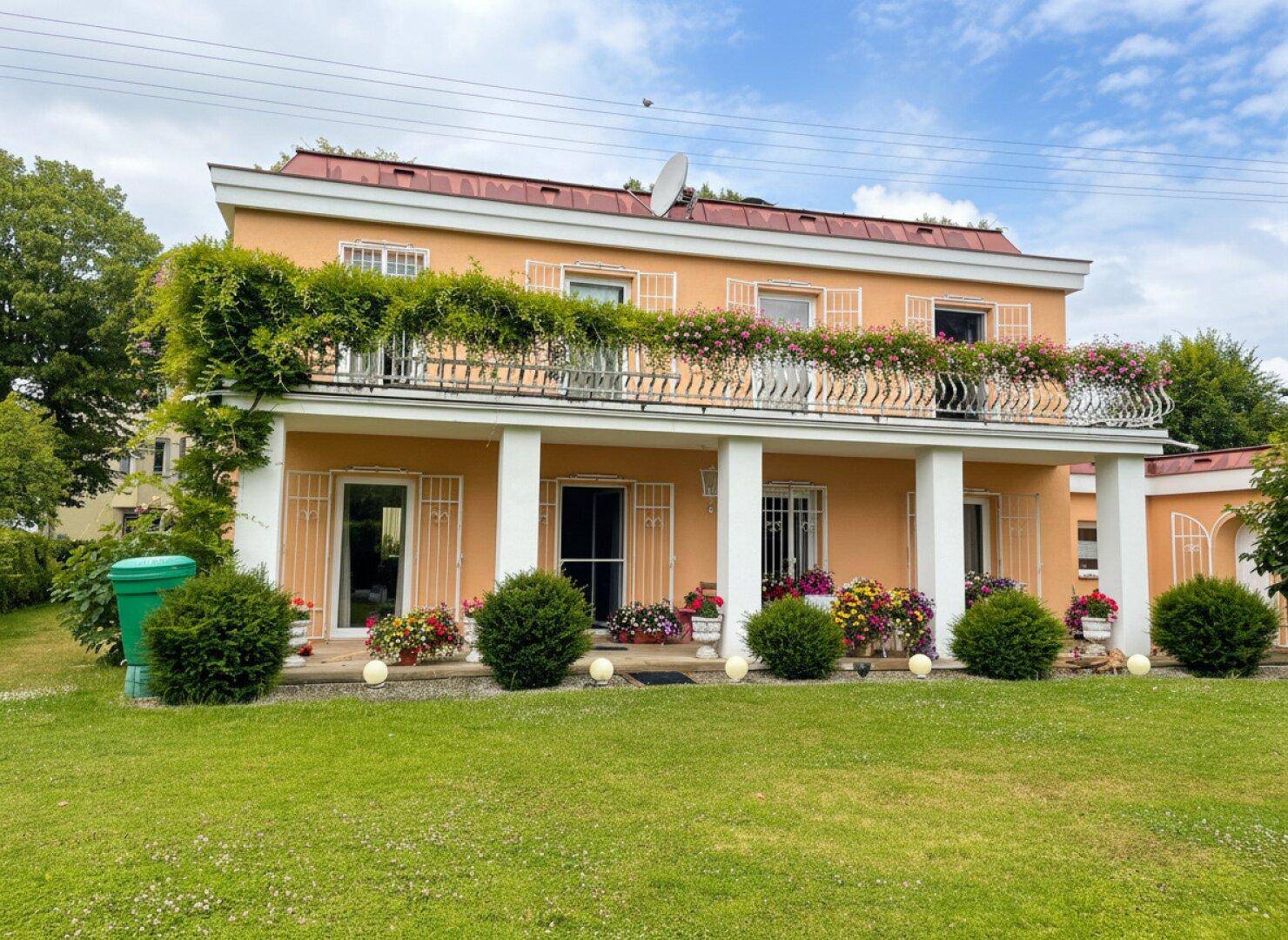 Charmantes Haus mit gepflegtem Vorgarten, Säulen und blühenden Blumenkästen, sehr einladend.