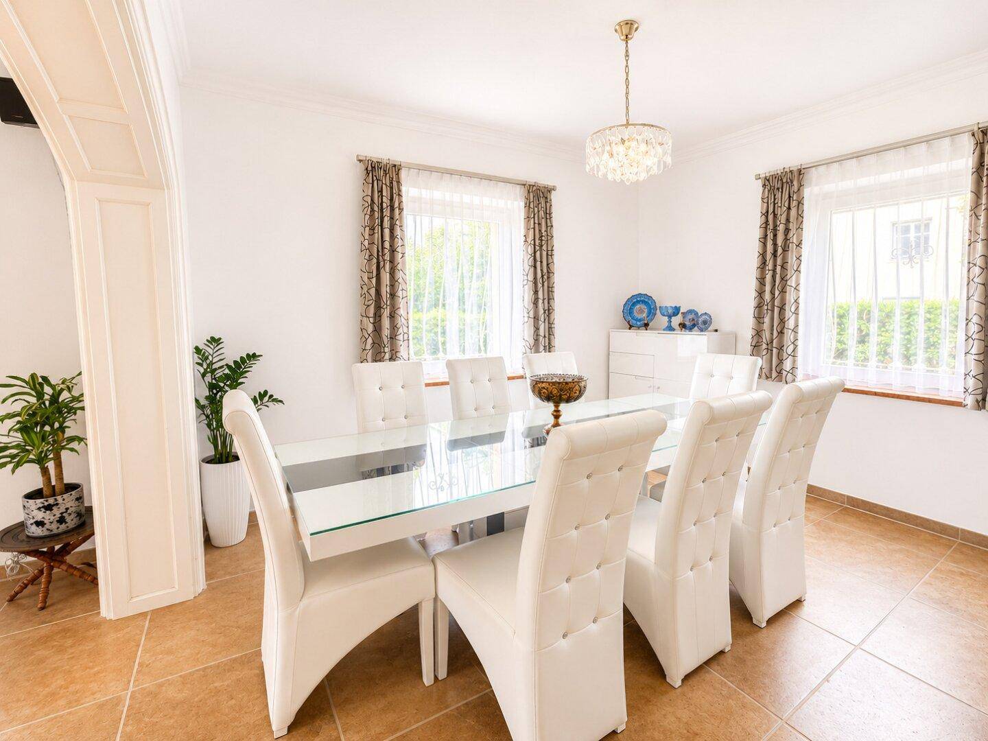 Eleganter Essbereich mit großem Glastisch, weißen Stühlen und funkelndem Kronleuchter, sehr stilvoll.