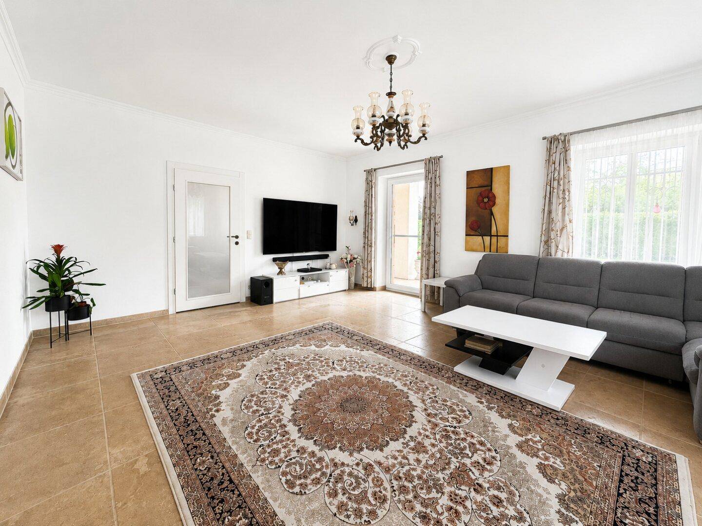 Helles Wohnzimmer mit großem Teppich, grauem Ecksofa und Zugang zur Terrasse, gemütlich und modern.