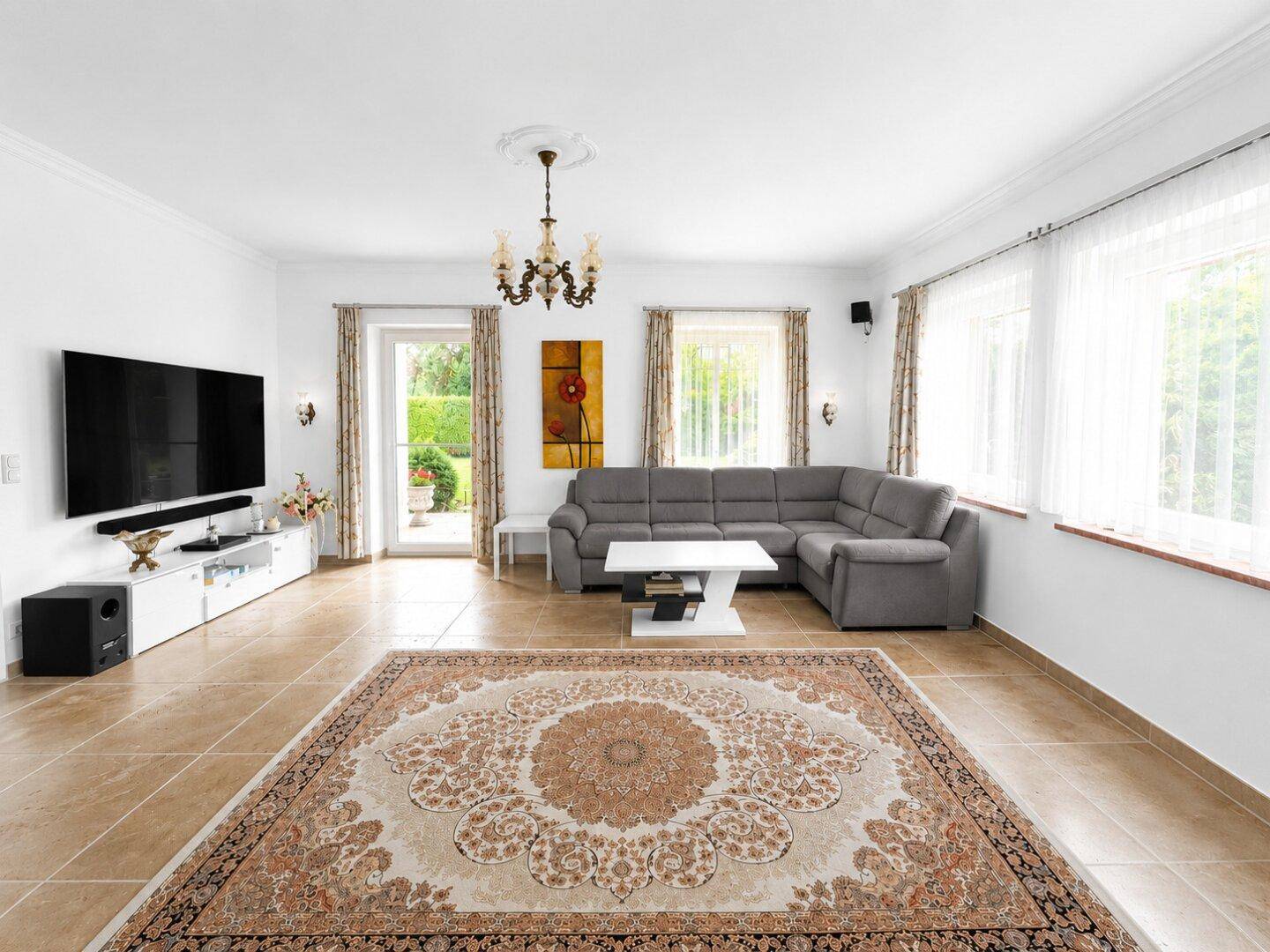 Geräumiges Wohnzimmer mit großem Teppich, bequemer Couch und Blick in den grünen Garten.