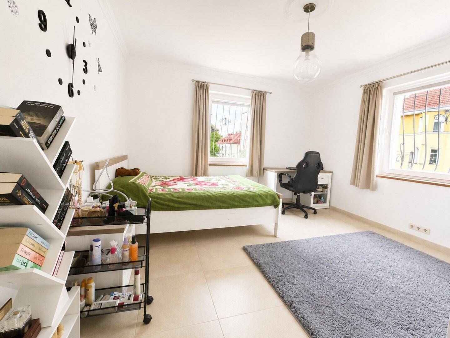 Schlafzimmer mit hellem Fliesenboden, Doppelbett und Schreibtisch am Fenster, ideal zum Arbeiten.