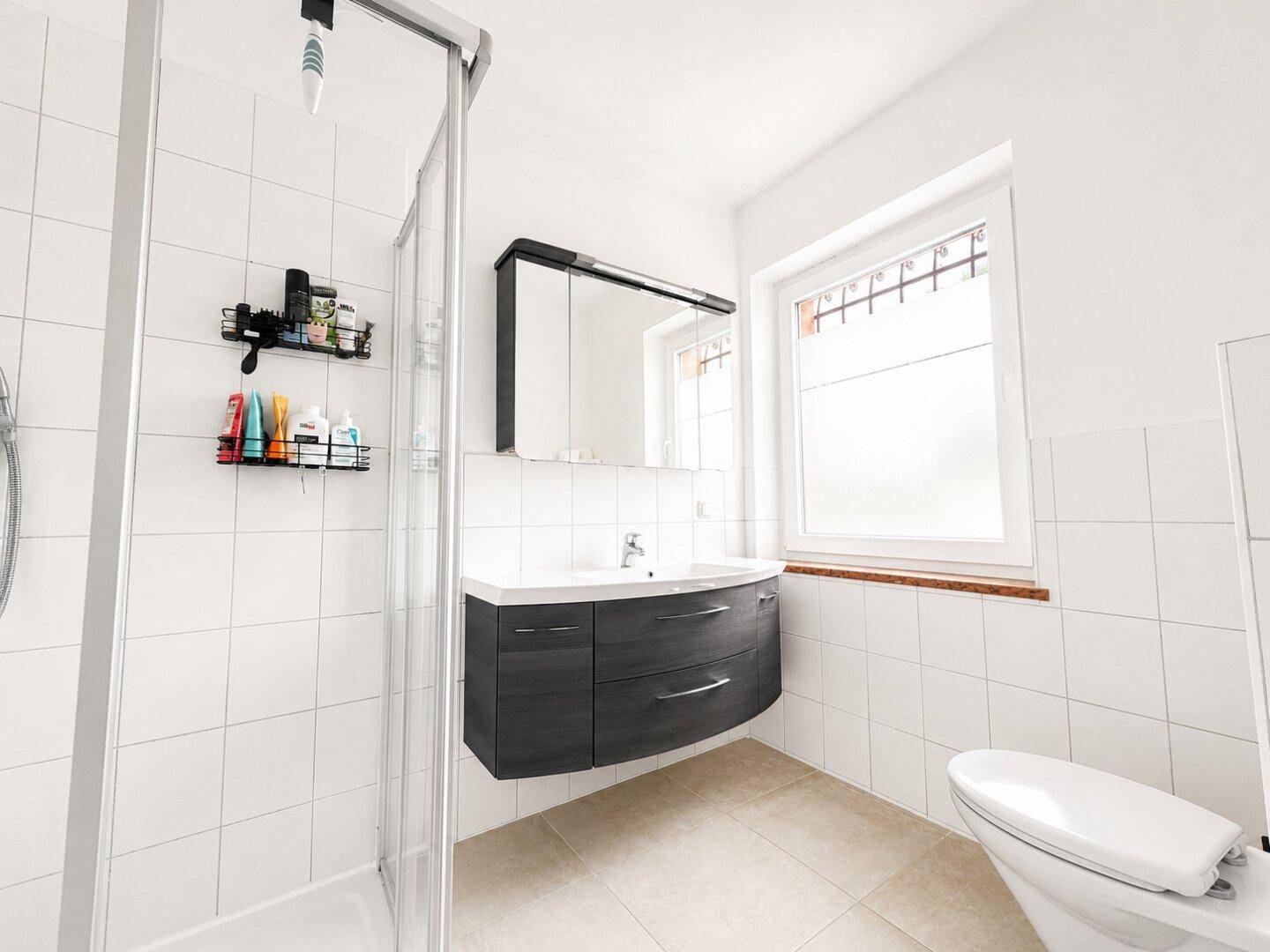 Modernes Badezimmer mit Dusche, Waschtisch und Fenster für Tageslicht, sauber und hell.