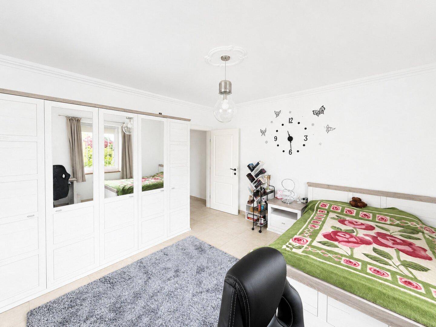 Helles Schlafzimmer mit großem Kleiderschrank, Doppelbett und dekorativer Wanduhr, gemütlich eingerichtet.