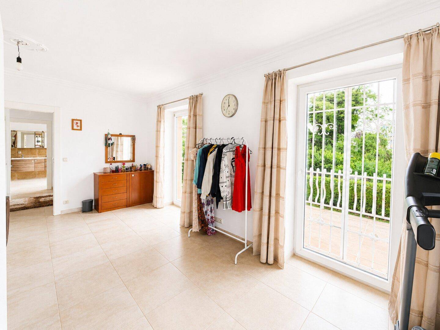 Heller Raum mit Fliesenboden, Kommode und Zugang zu einem französischen Balkon, vielseitig nutzbar.