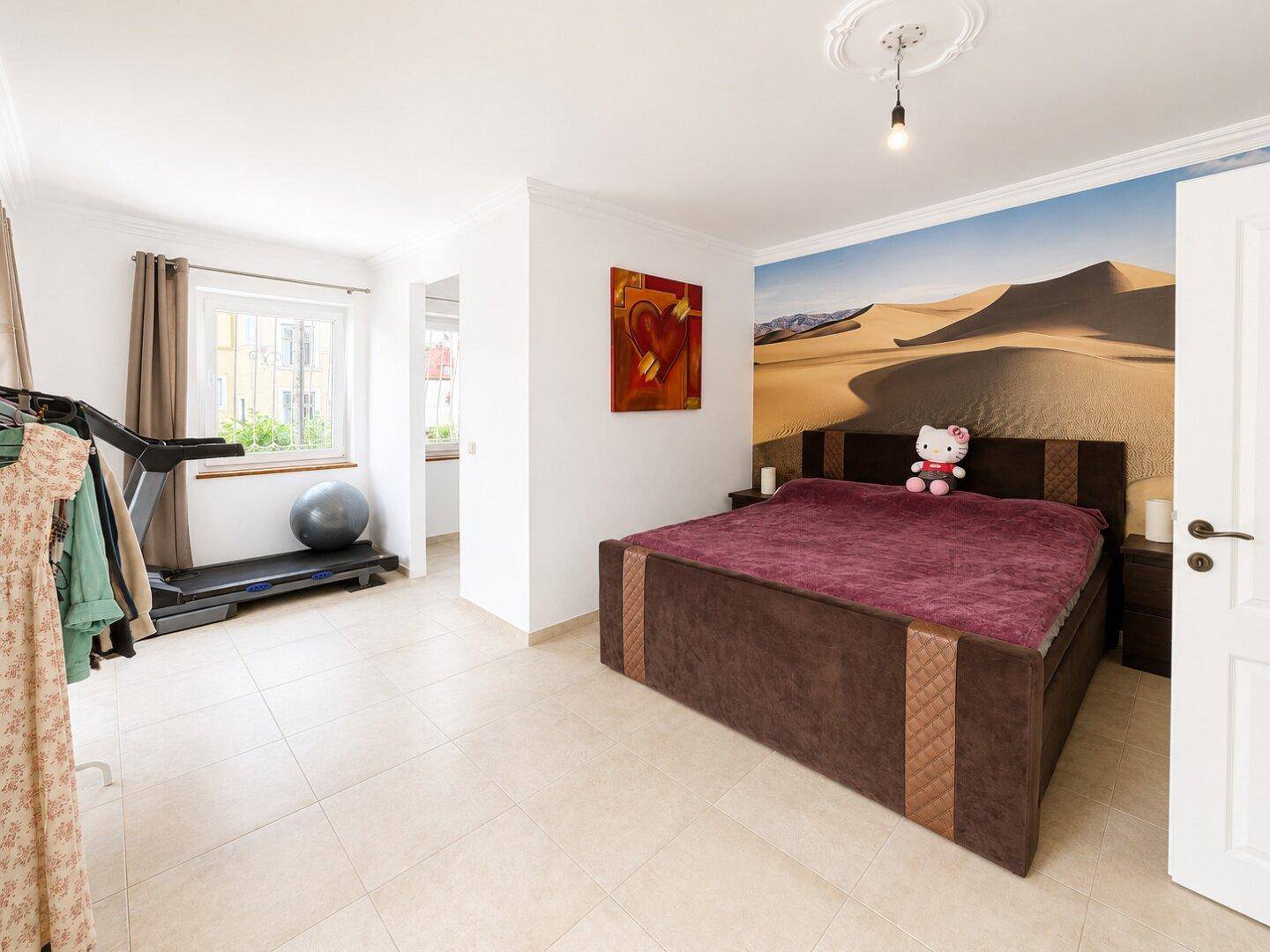 Schlafzimmer mit Doppelbett, Laufband und dekorativer Wüsten-Fototapete, individuell gestaltet.