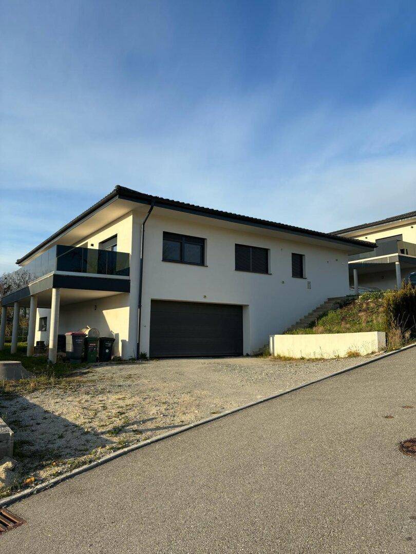 Modernes Einfamilienhaus mit Garage, Balkon und Zufahrt in ländlicher Umgebung.