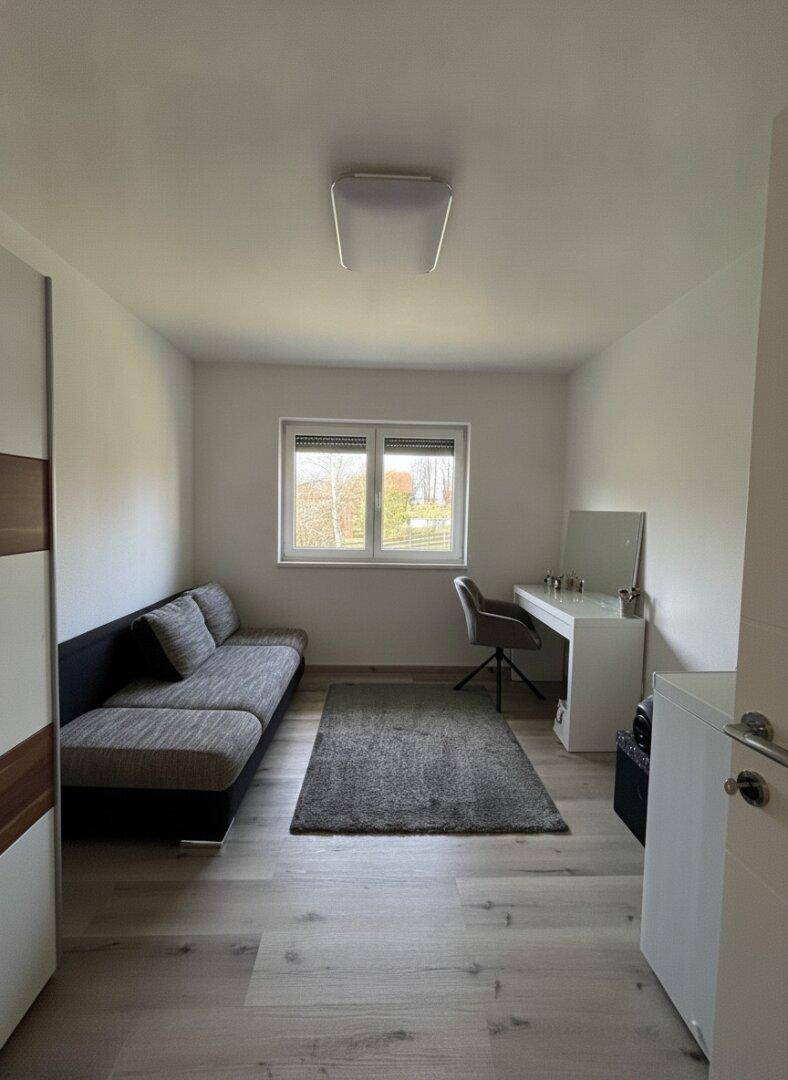 Schlichtes Schlafzimmer mit Schlafsofa, Schreibtisch und hellem Laminatboden.