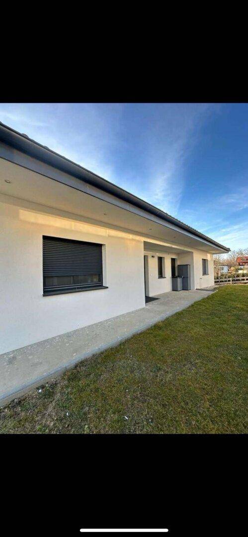 Seitenansicht des modernen Hauses mit weißer Fassade und grüner Rasenfläche.