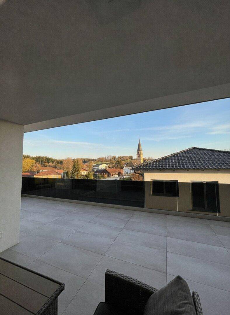 Weitblick von der Terrasse über ein Dorf mit Kirchturm und umliegender Landschaft.