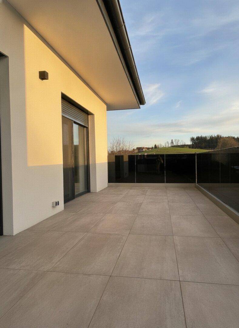 Sonnige Terrasse mit Fliesenboden und weitem Blick ins Grüne und die Landschaft.
