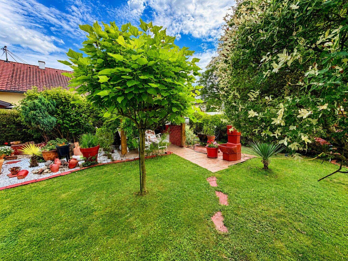 Gepflegter Garten mit Rasenfläche, dekorativen Elementen und einem kleinen Baum in der Mitte.