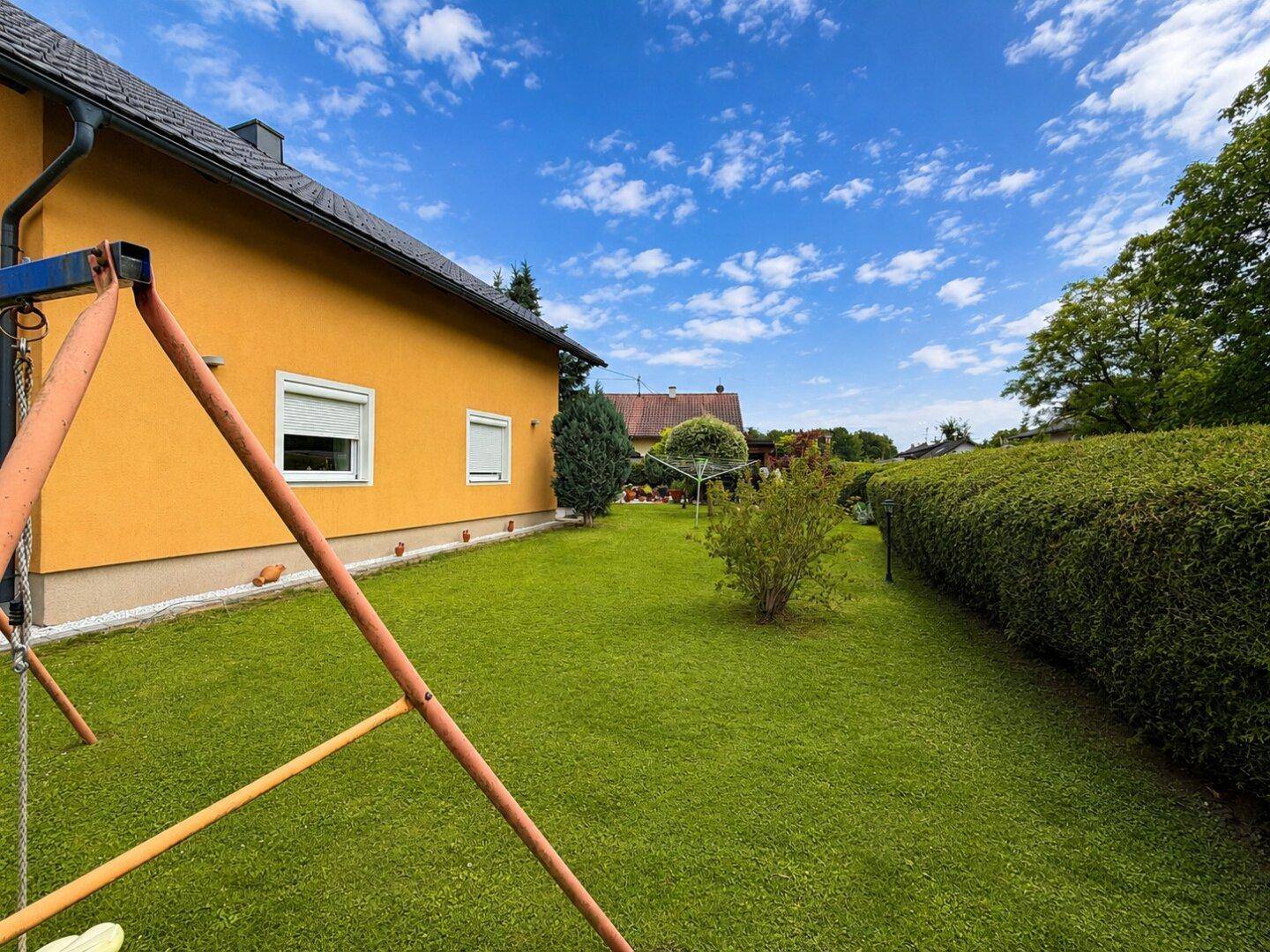 Seitenansicht des Hauses mit gelber Fassade, grüner Rasenfläche und einem Schaukelgestell.