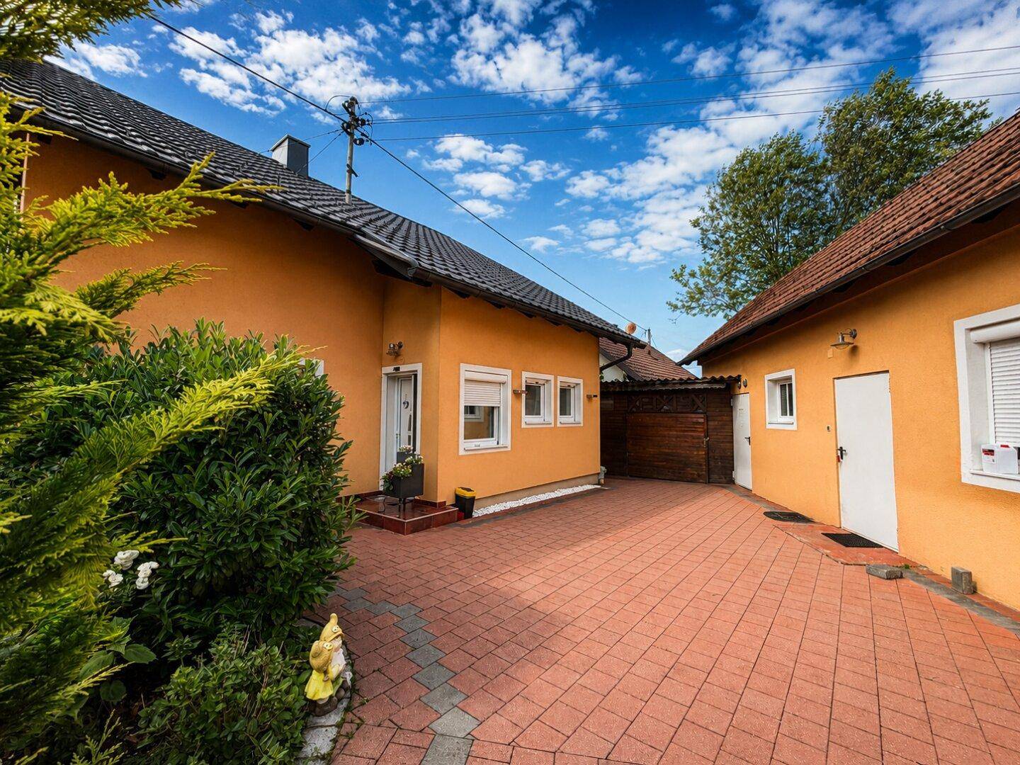 Vorderansicht des Hauses mit gepflasterter Einfahrt und einem Nebengebäude im Hintergrund.