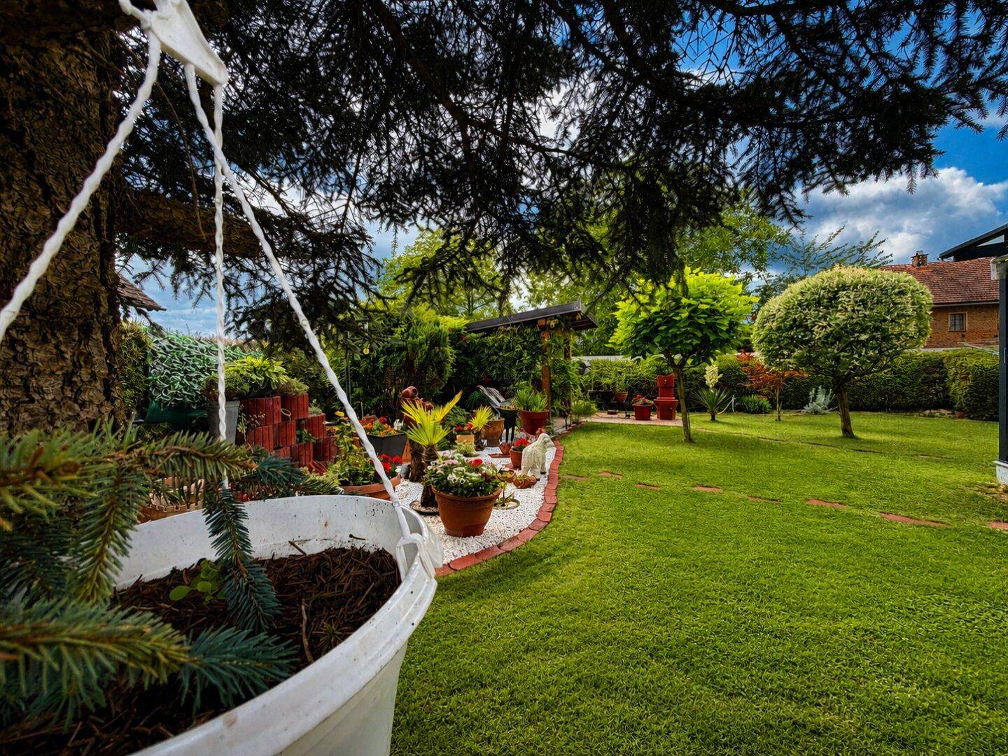 Idyllischer Gartenbereich mit üppiger Bepflanzung, Blumenkübeln und einem großen Baum.