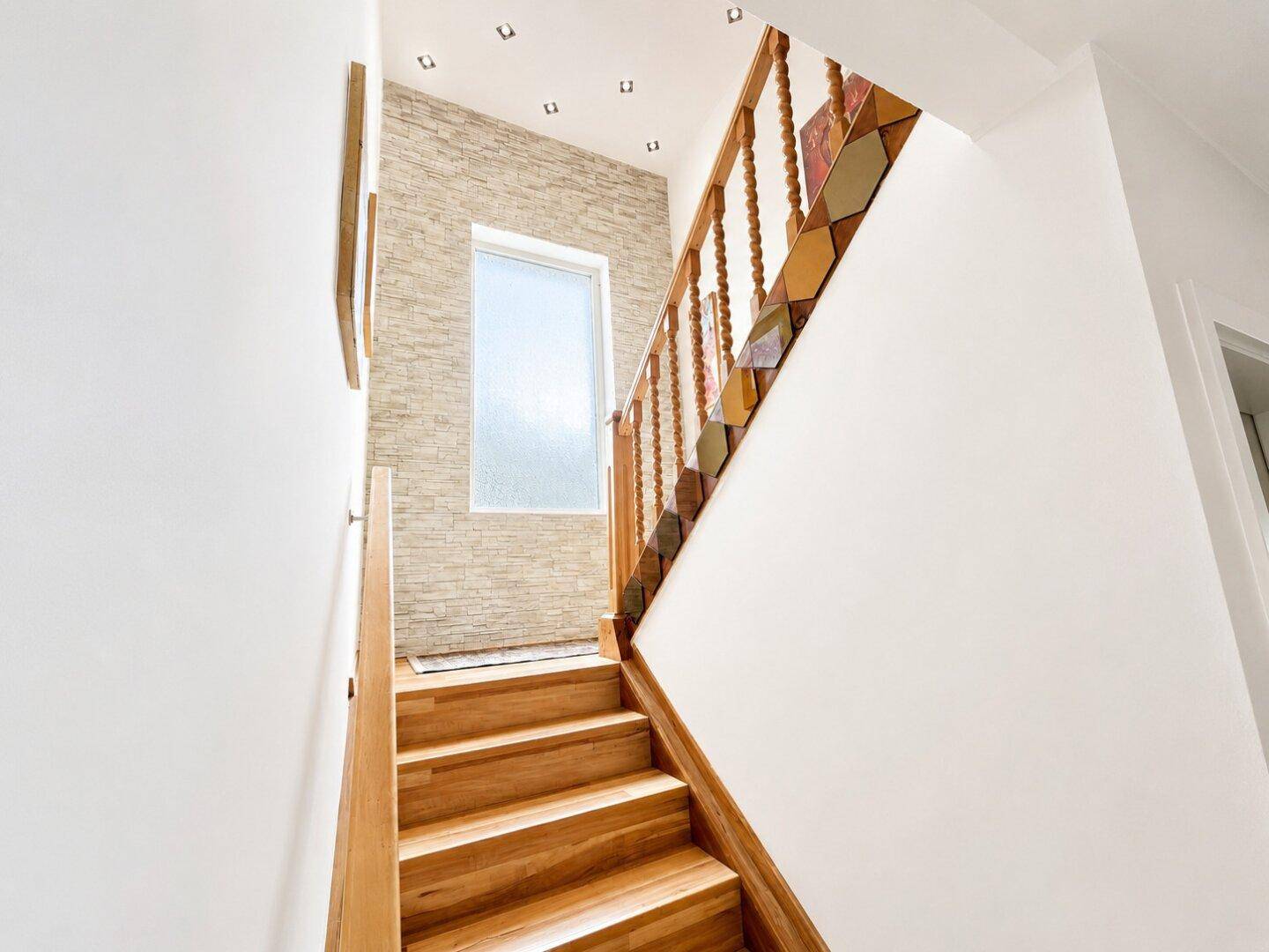 Heller Treppenaufgang mit Holzstufen, dekorativer Steinwand und natürlichem Lichteinfall.