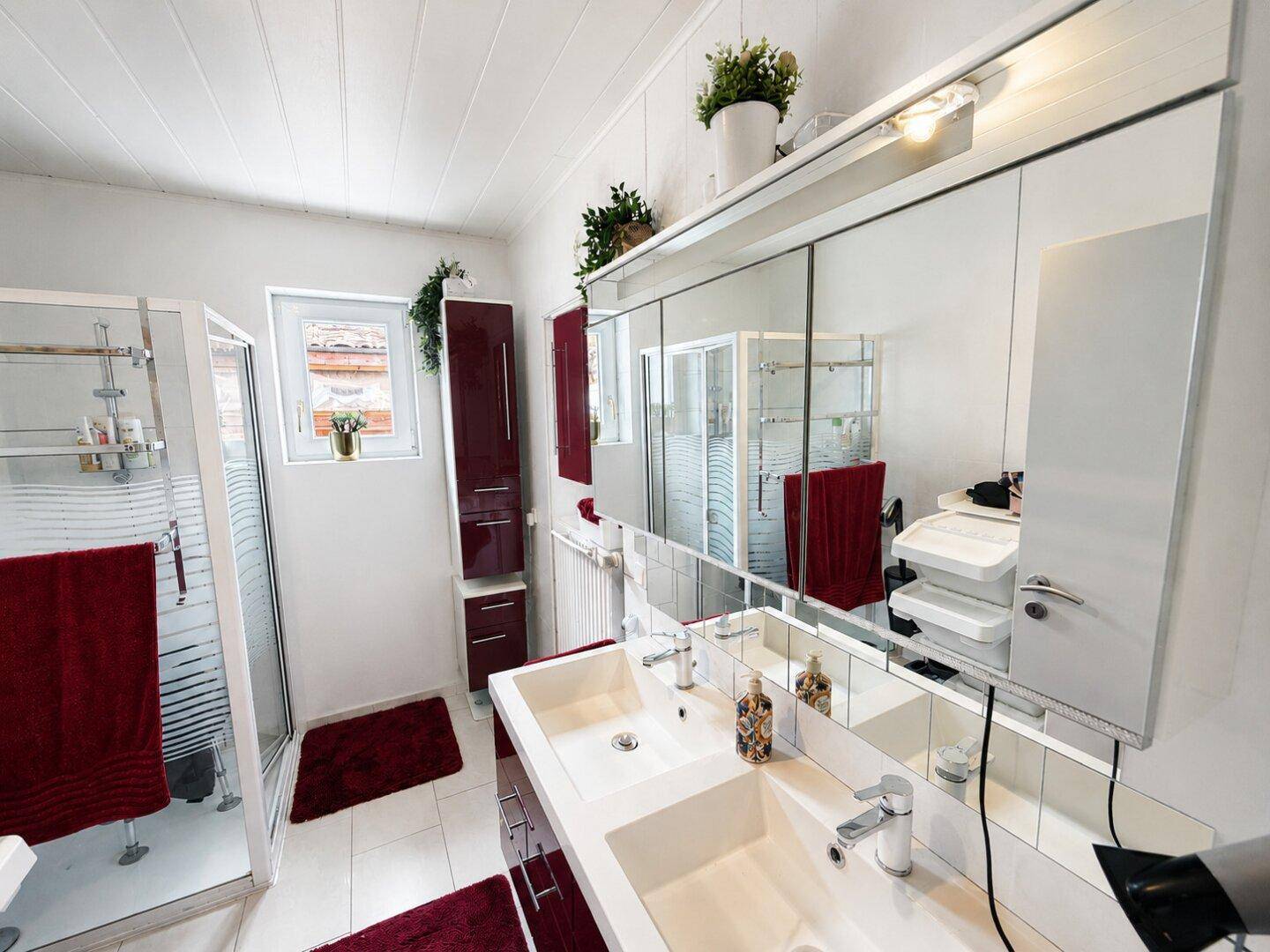 Modernes Badezimmer mit Doppelwaschbecken, großer Spiegelfront und Duschkabine.