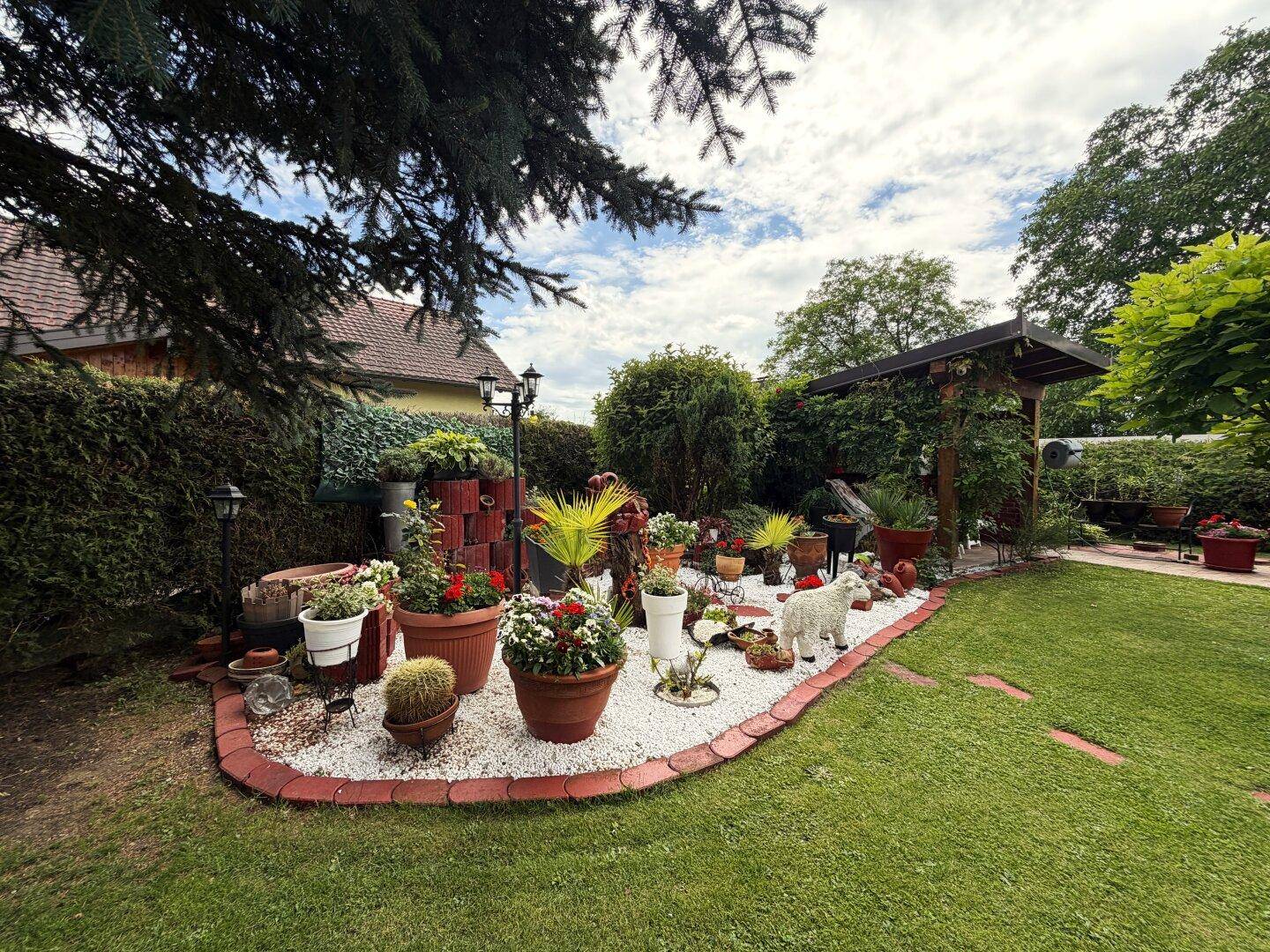 Attraktiver Gartenbereich mit gepflegtem Rasen, Blumenbeeten und einem überdachten Sitzbereich.