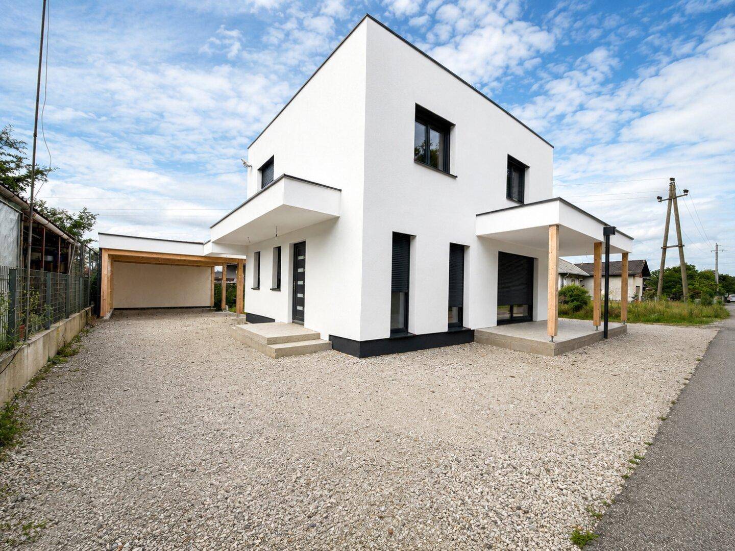 Freistehendes modernes Haus mit weißer Fassade, Carport und großzügiger Kiesauffahrt.