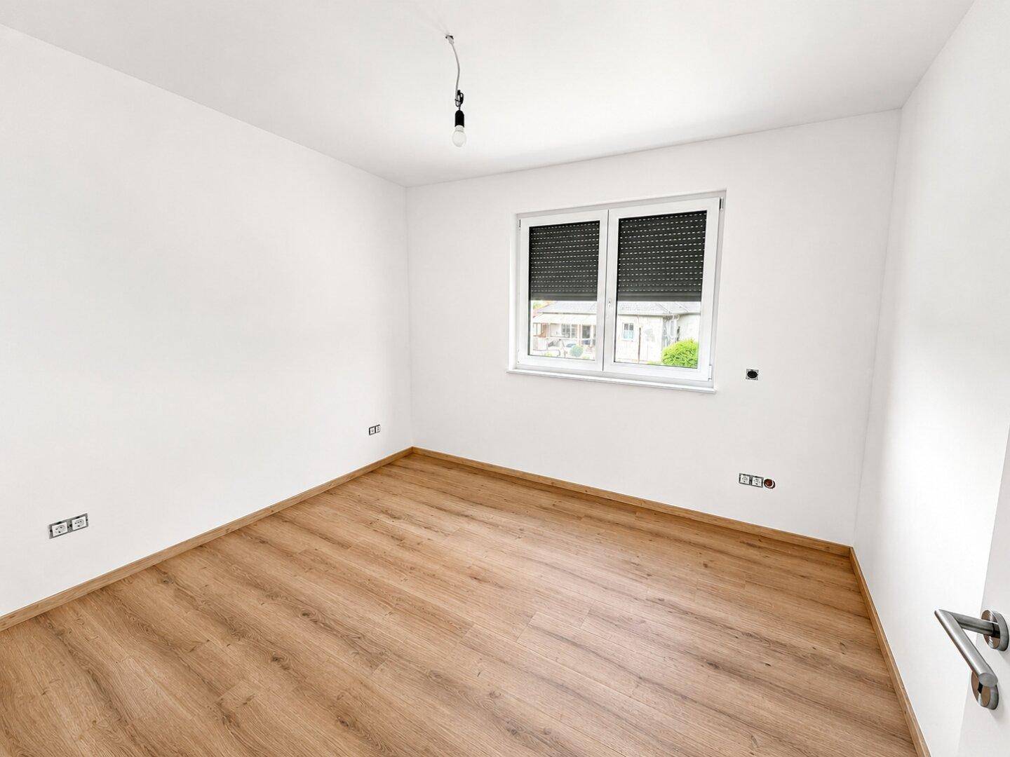 Helles Schlafzimmer mit Laminatboden, weißen Wänden und Fenster mit Rollladen.