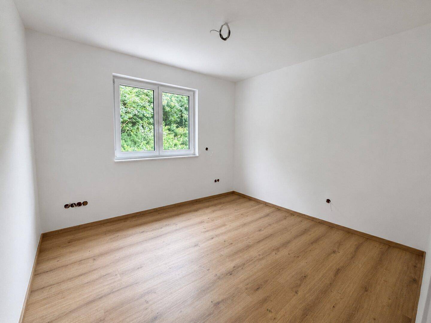 Geräumiges Schlafzimmer mit Laminatboden, weißen Wänden und Blick ins Grüne.