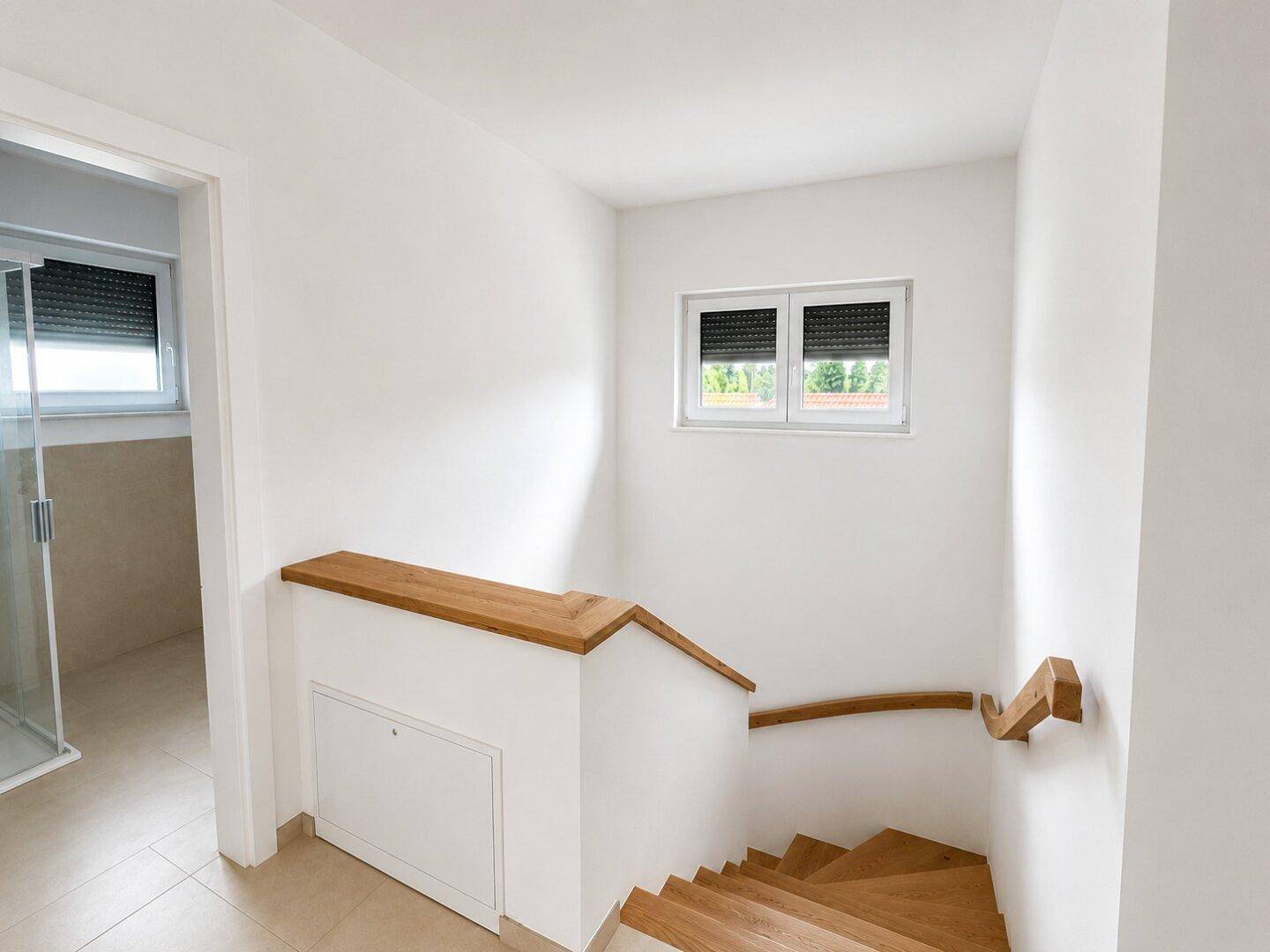 Oberer Treppenabsatz mit Holzgeländer, Fenster und Blick in ein angrenzendes Badezimmer.