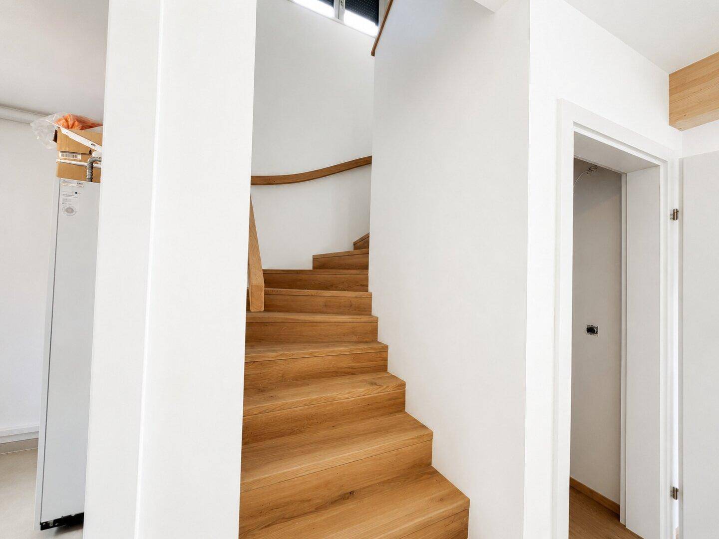Elegante Holztreppe mit geschwungenem Geländer in einem hellen Treppenhaus.