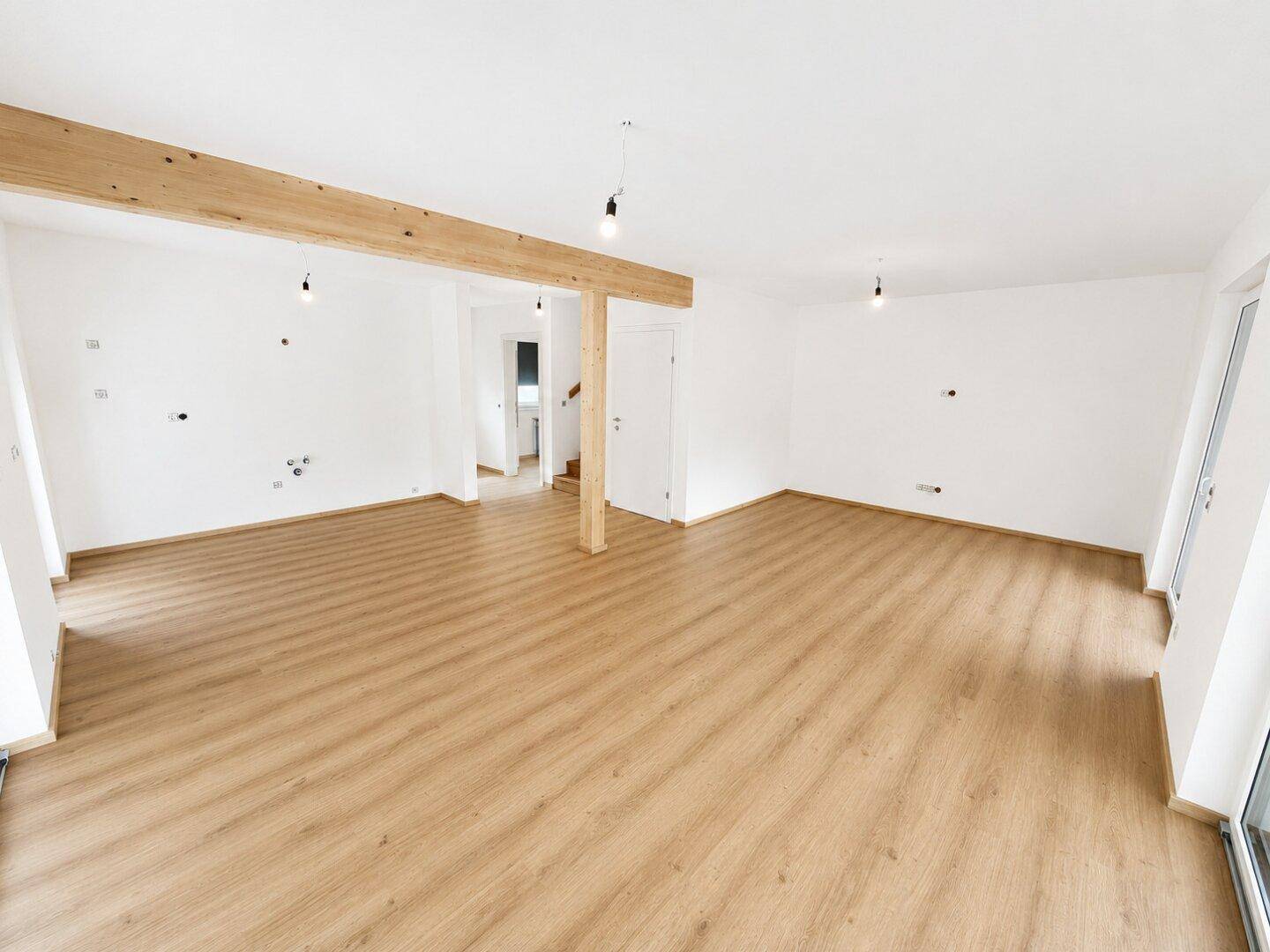 Heller, leerer Wohnbereich mit Holzbalken, Laminatboden und weißen Wänden, bereit zur Einrichtung.