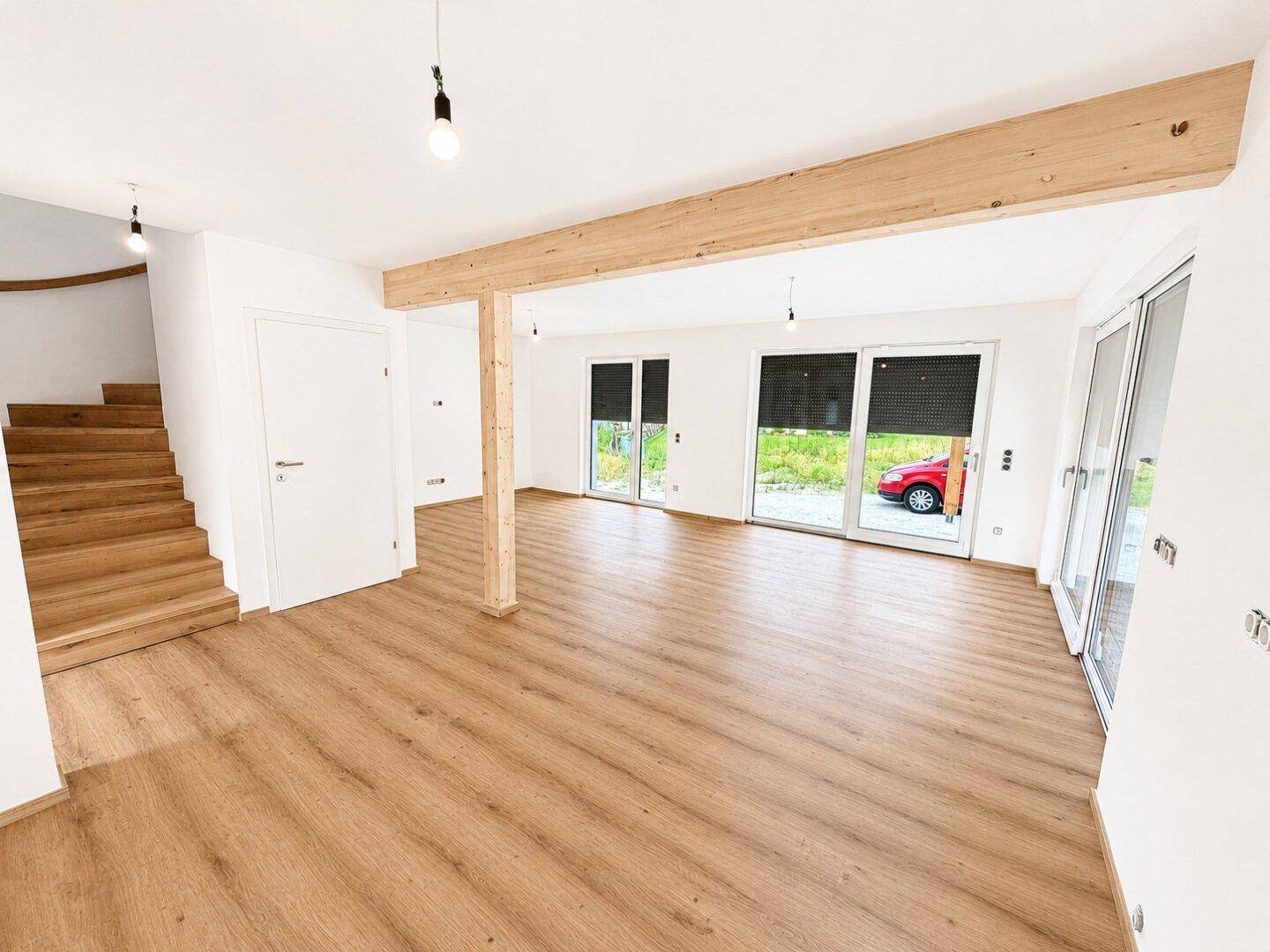 Geräumiger Wohnbereich mit Laminatboden, Holzbalken und Zugang zur Holztreppe.