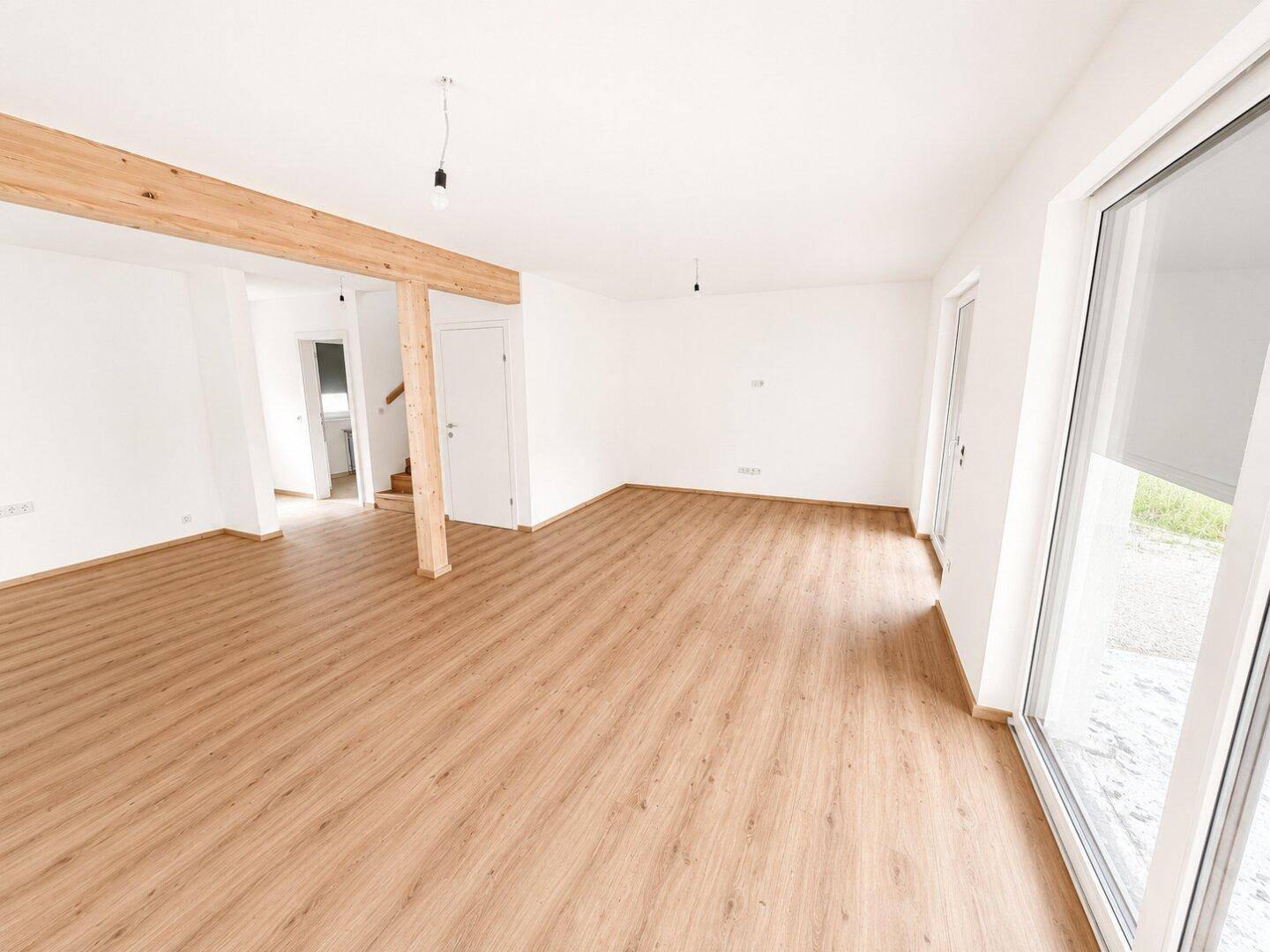 Weitläufiger, heller Wohnbereich mit Laminatboden und großen Fenstern, die viel Licht hereinlassen.