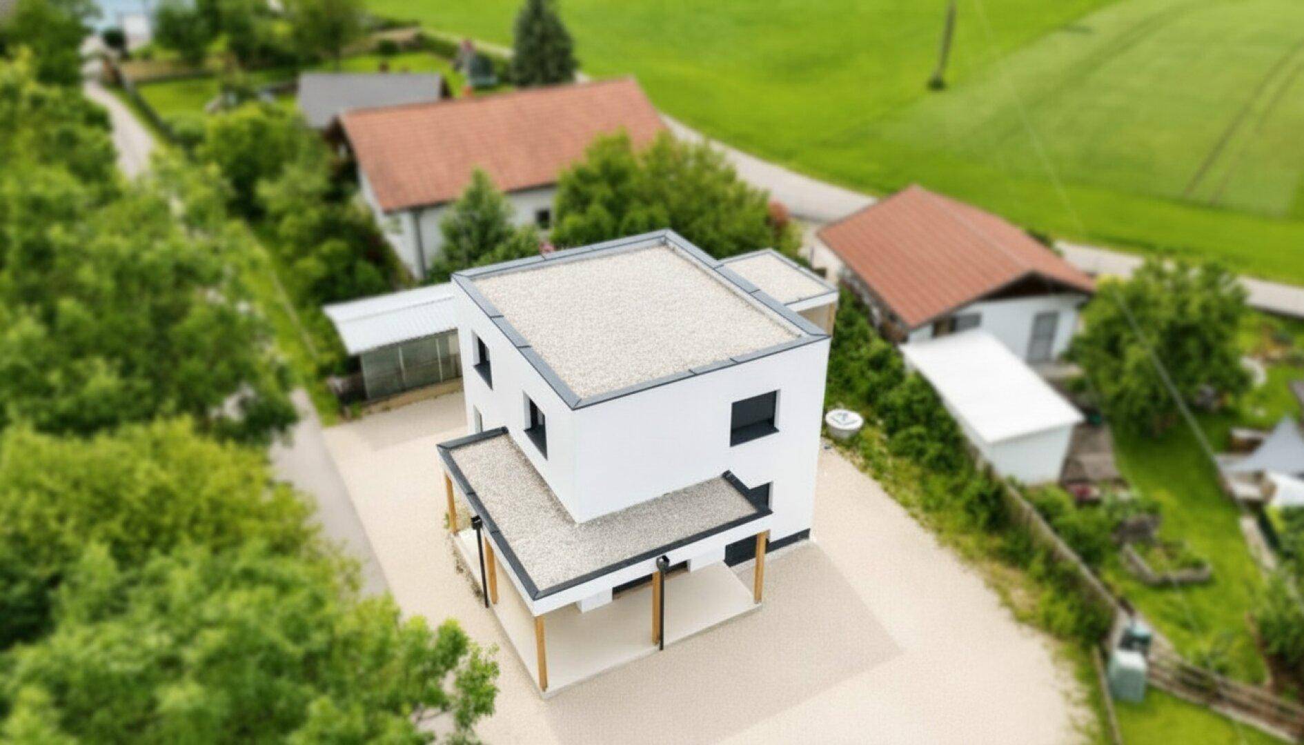 Luftaufnahme eines modernen Einfamilienhauses mit Flachdach und umliegender grüner Landschaft.