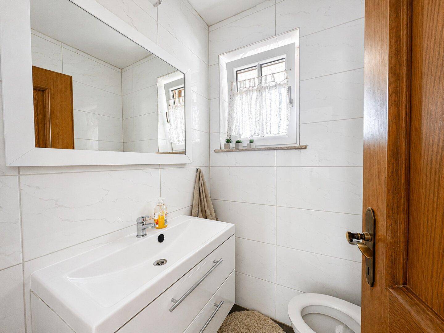 Modernes Gäste-WC mit weißen Fliesen, einem Waschbecken und einem kleinen Fenster.