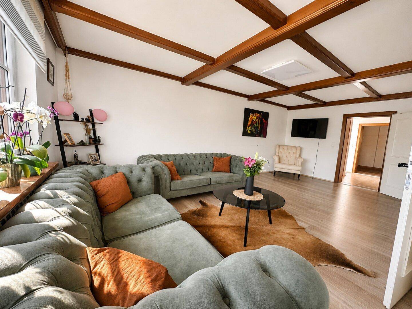 Gemütliches Wohnzimmer mit sichtbaren Holzbalken an der Decke und großem, bequemen Sofa.