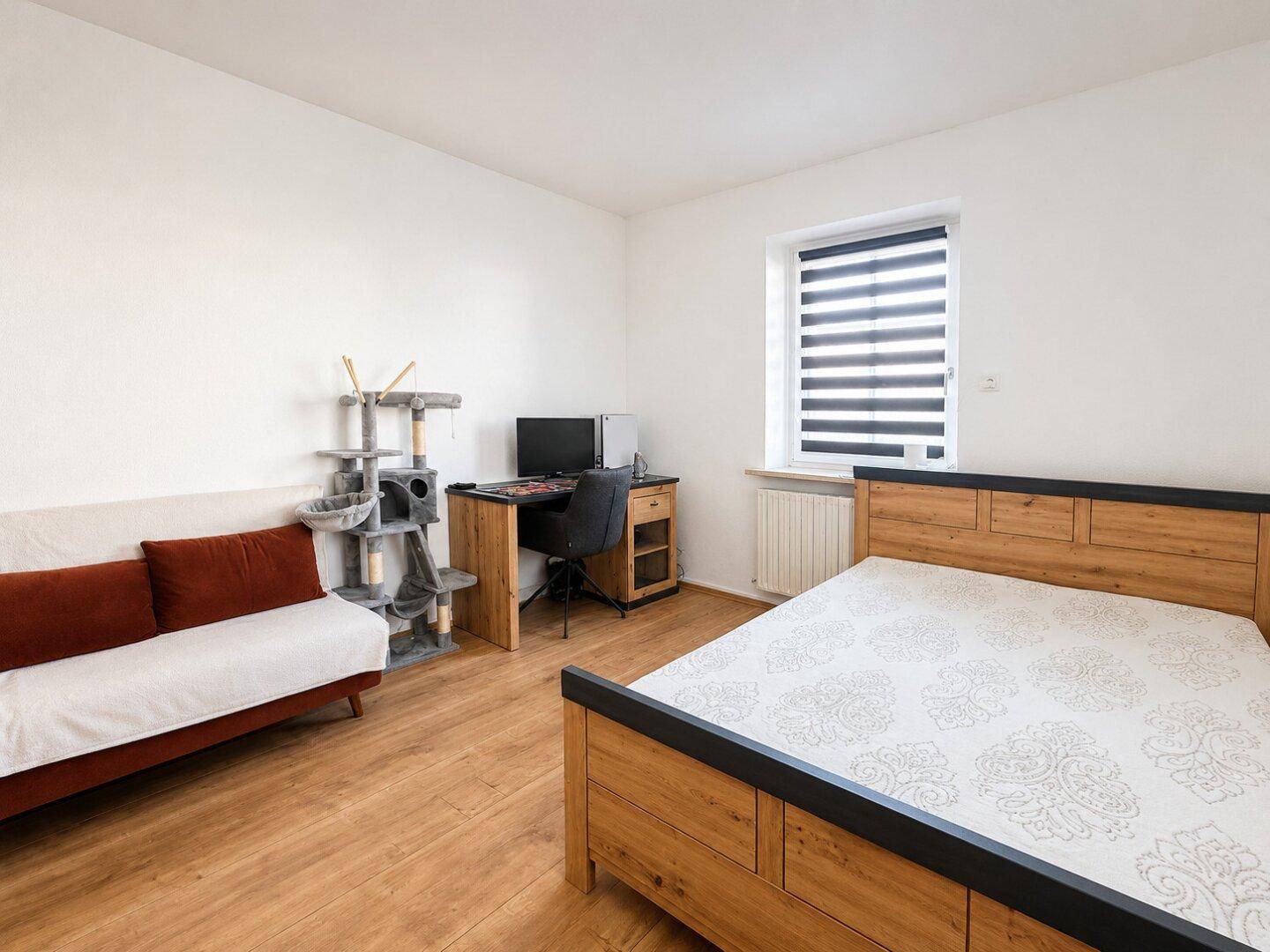 Helles Schlafzimmer mit Bett, Schreibtisch und kleinem Sofa, ideal als Gäste- oder Kinderzimmer.