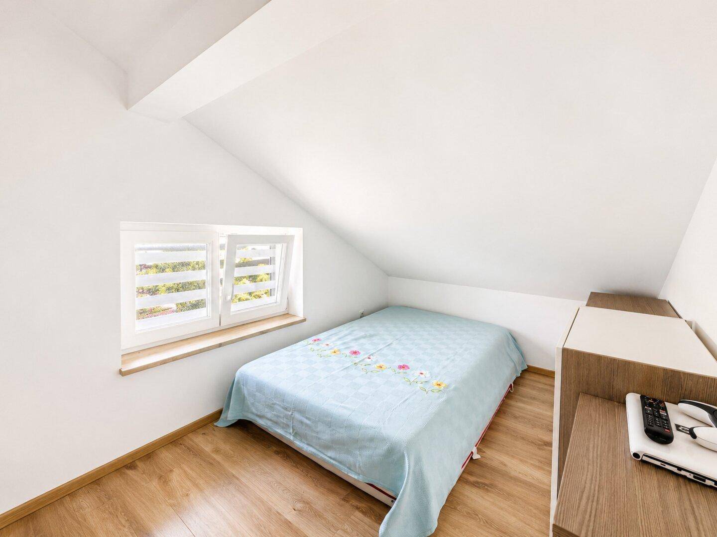 Gemütliches Schlafzimmer im Dachgeschoss mit schräger Decke, Einzelbett und kleinem Fenster.