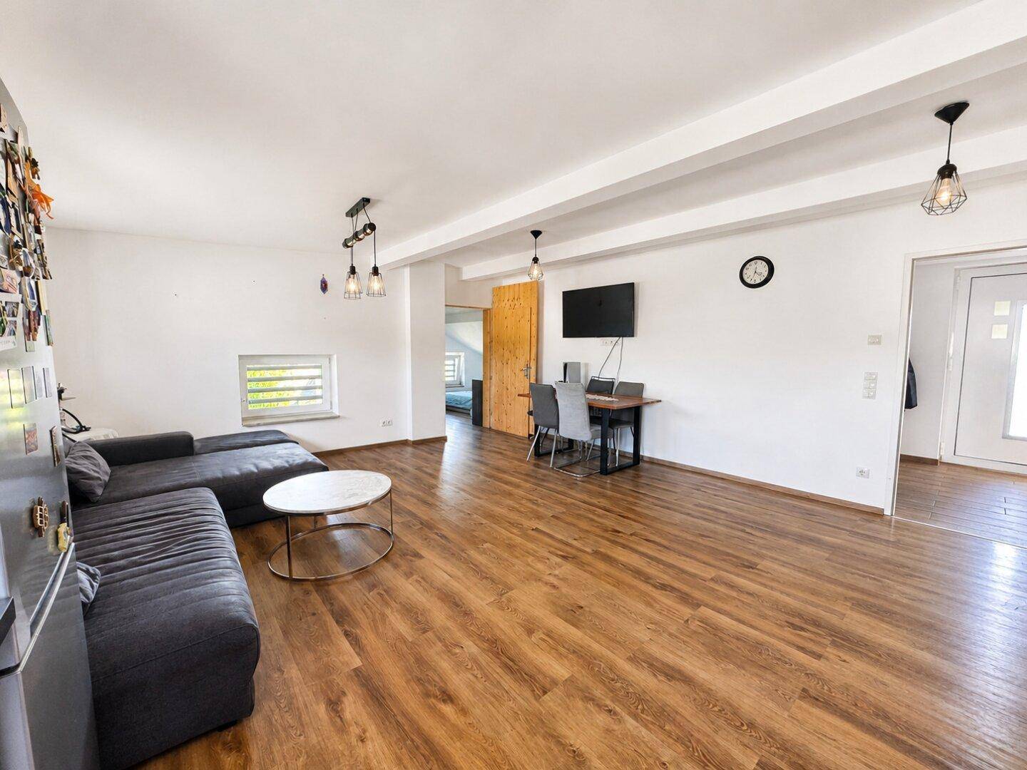 Geräumiges Wohnzimmer mit dunklem Laminatboden, großem Ecksofa und integriertem Arbeitsbereich.