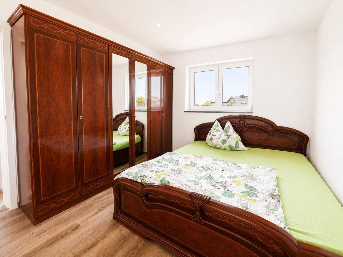 Schlafzimmer mit klassischem Holzbett und großem Kleiderschrank mit Spiegeltüren.