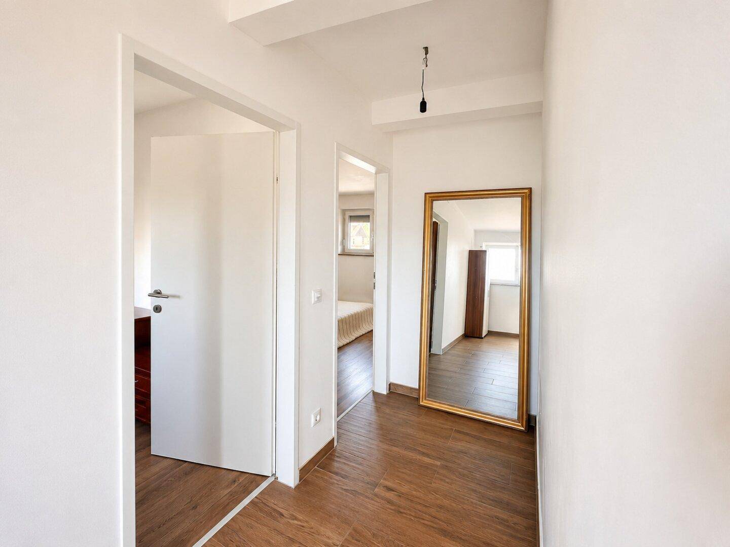 Heller Flur mit Holzboden und einem großen Standspiegel, der den Zugang zu weiteren Zimmern zeigt.