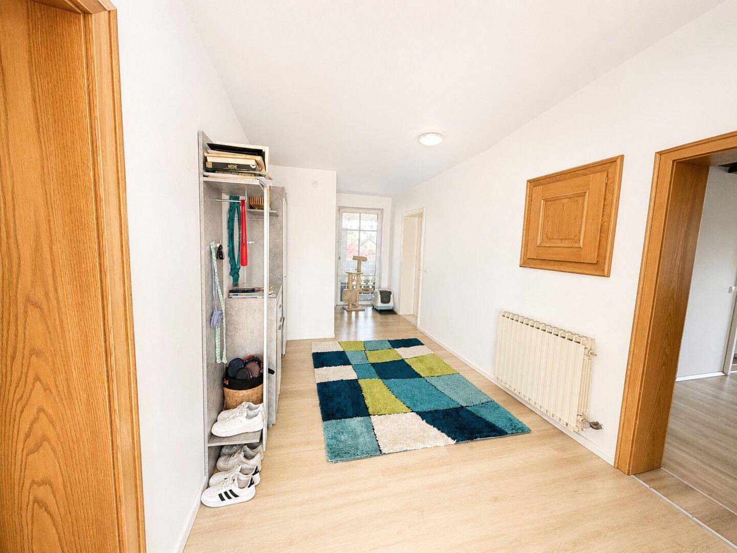 Heller Flur mit Laminatboden, einer Garderobe und einem farbenfrohen Teppich.