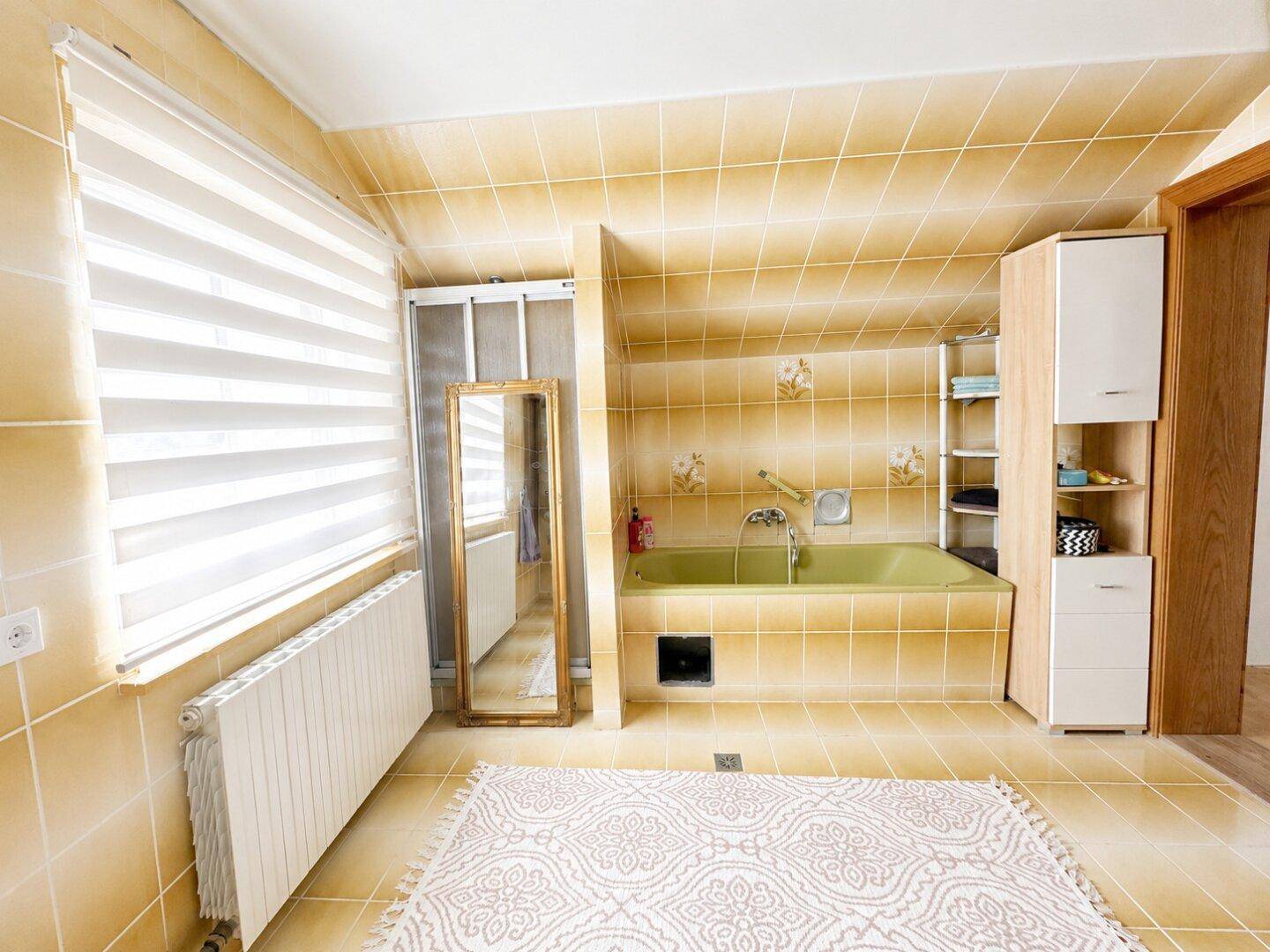 Badezimmer mit gelben Fliesen, einer grünen Badewanne und einem Heizkörper unter dem Fenster.