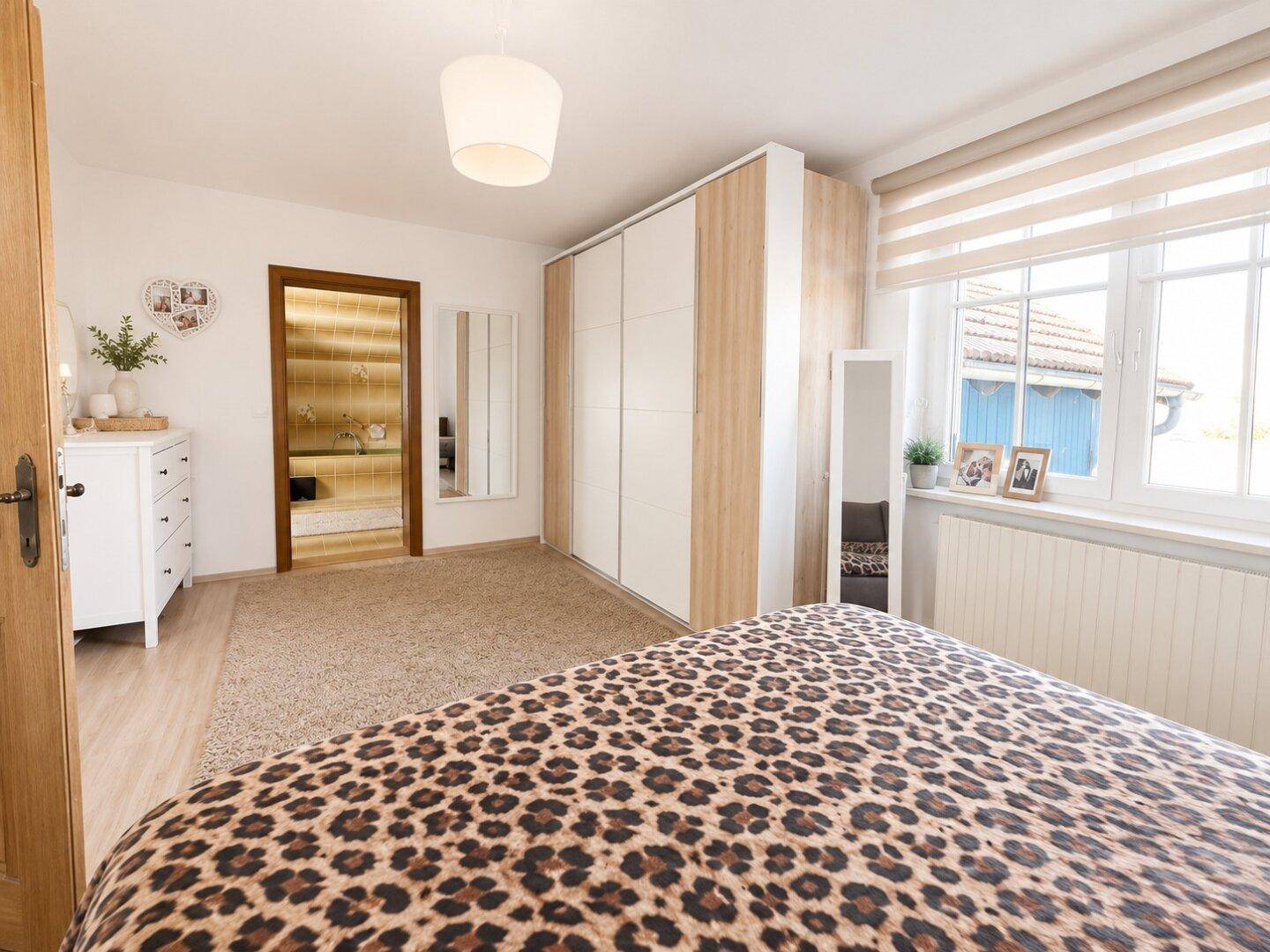 Schlafzimmer mit auffälliger Bettwäsche, großem Kleiderschrank und Fenster mit Blick ins Grüne.