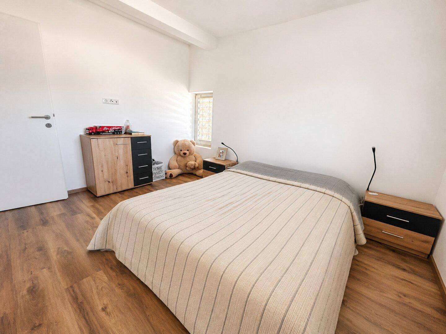 Geräumiges Schlafzimmer mit Doppelbett, Kommode und hellem Laminatboden.