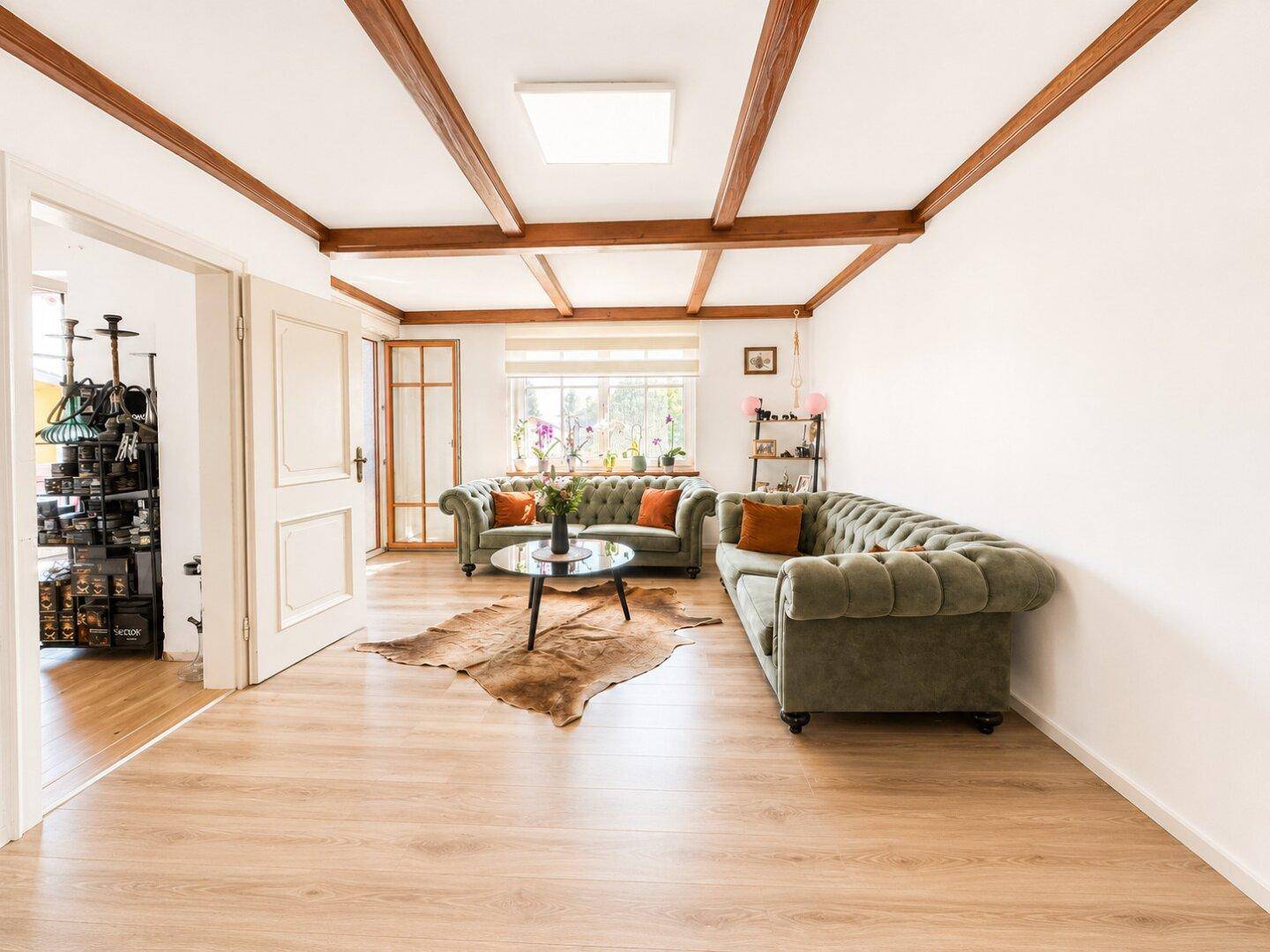 Helles Wohnzimmer mit Holzbalken an der Decke, bequemen Sofas und viel Tageslicht.
