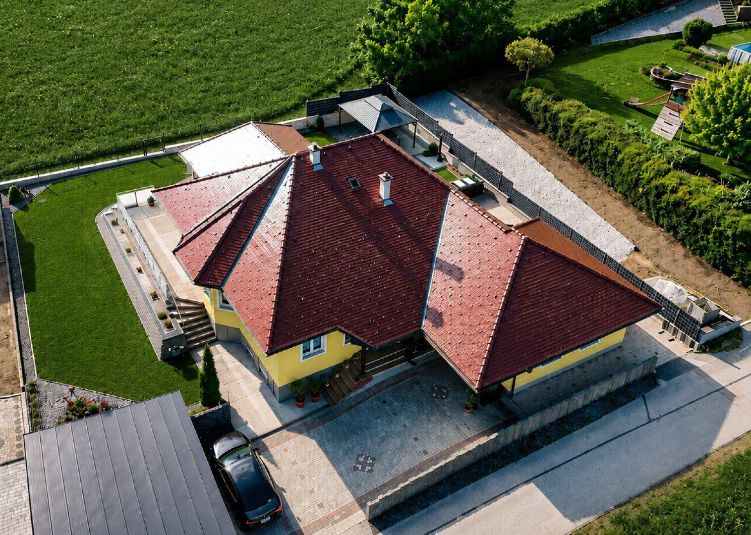 Luftaufnahme des Hauses mit rotem Dach, gelber Fassade und gepflasterter Einfahrt.