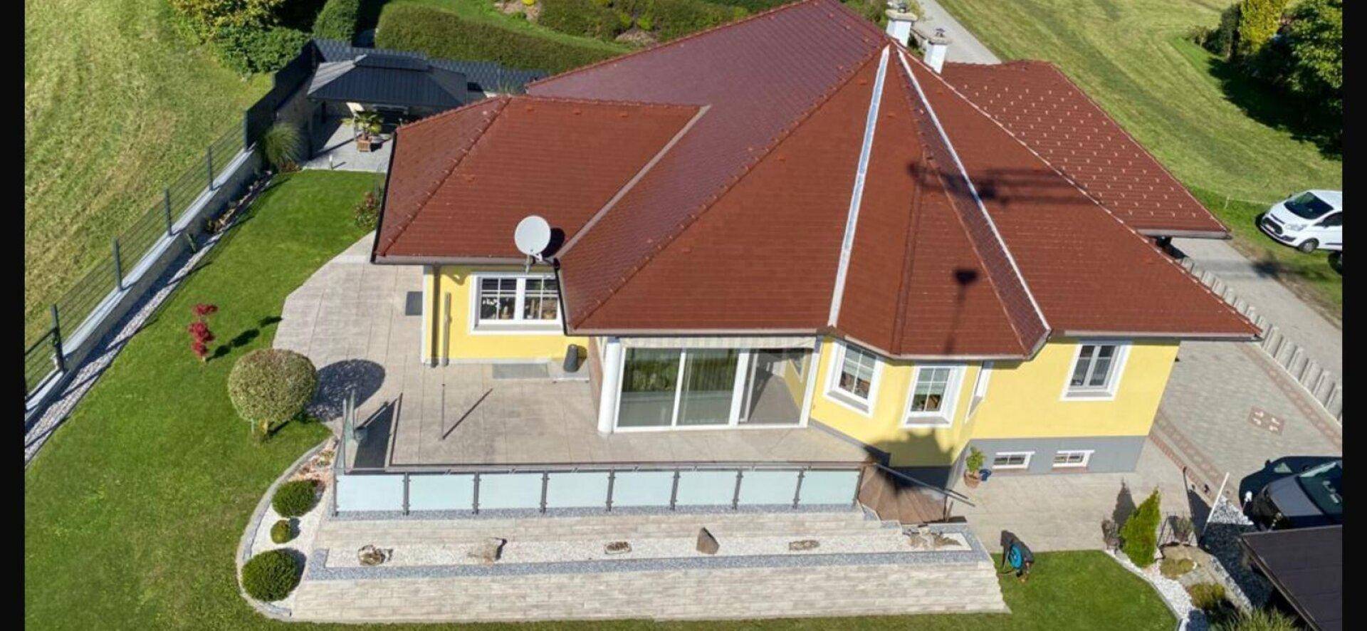 Luftaufnahme des Hauses mit großer Terrasse, rotem Dach und gepflegtem Garten.