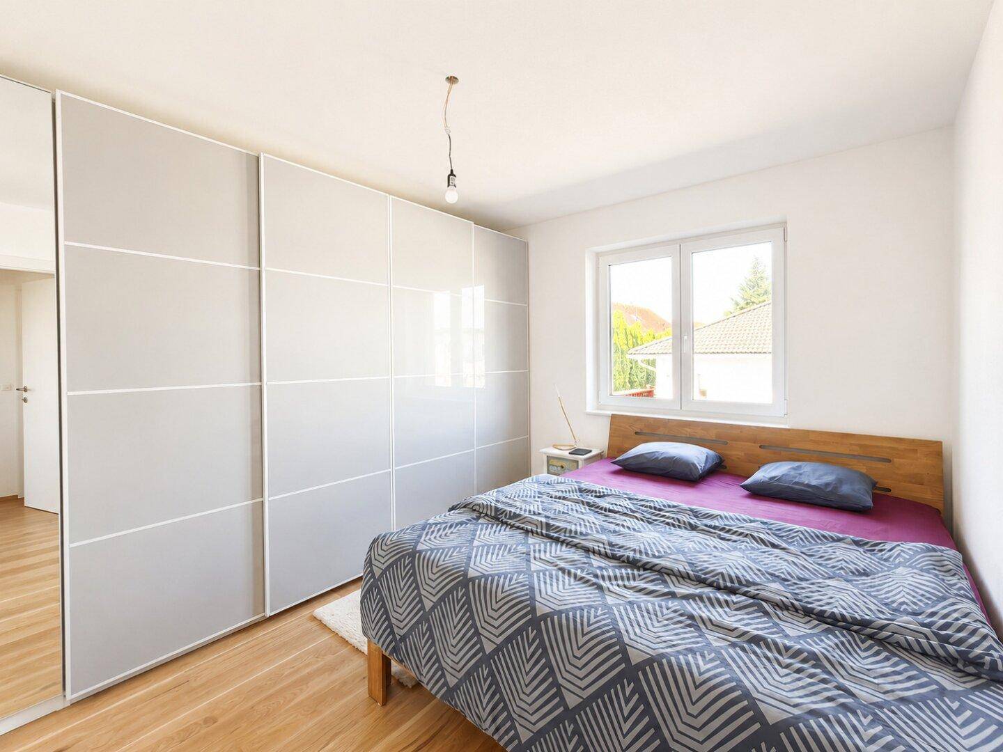 Gemütliches Schlafzimmer mit Holzbett, großem Kleiderschrank und viel Tageslicht durch das Fenster.