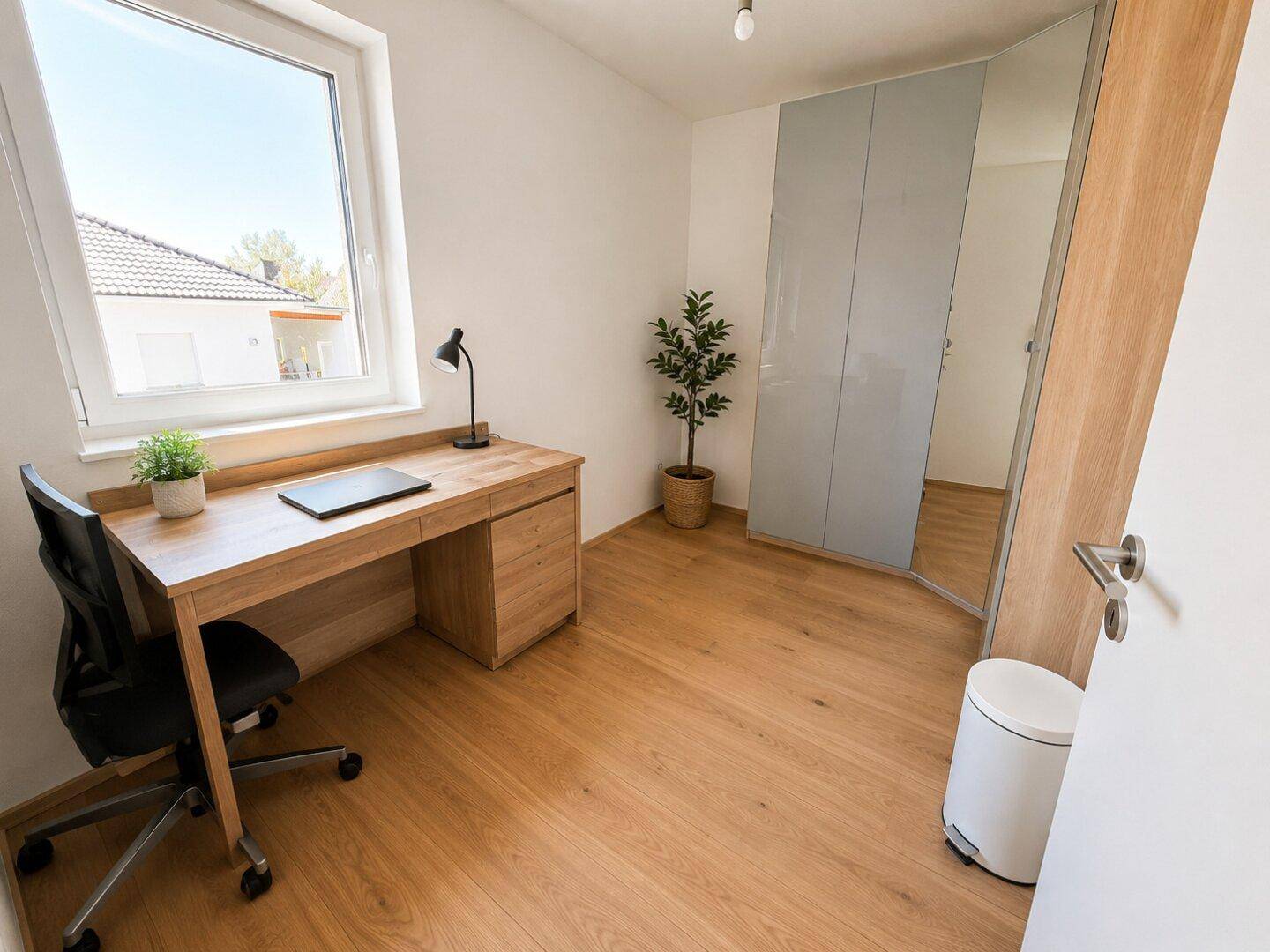 Ruhiges Arbeitszimmer mit Holzboden, Schreibtisch und großem Fenster für eine angenehme Arbeitsatmosphäre.