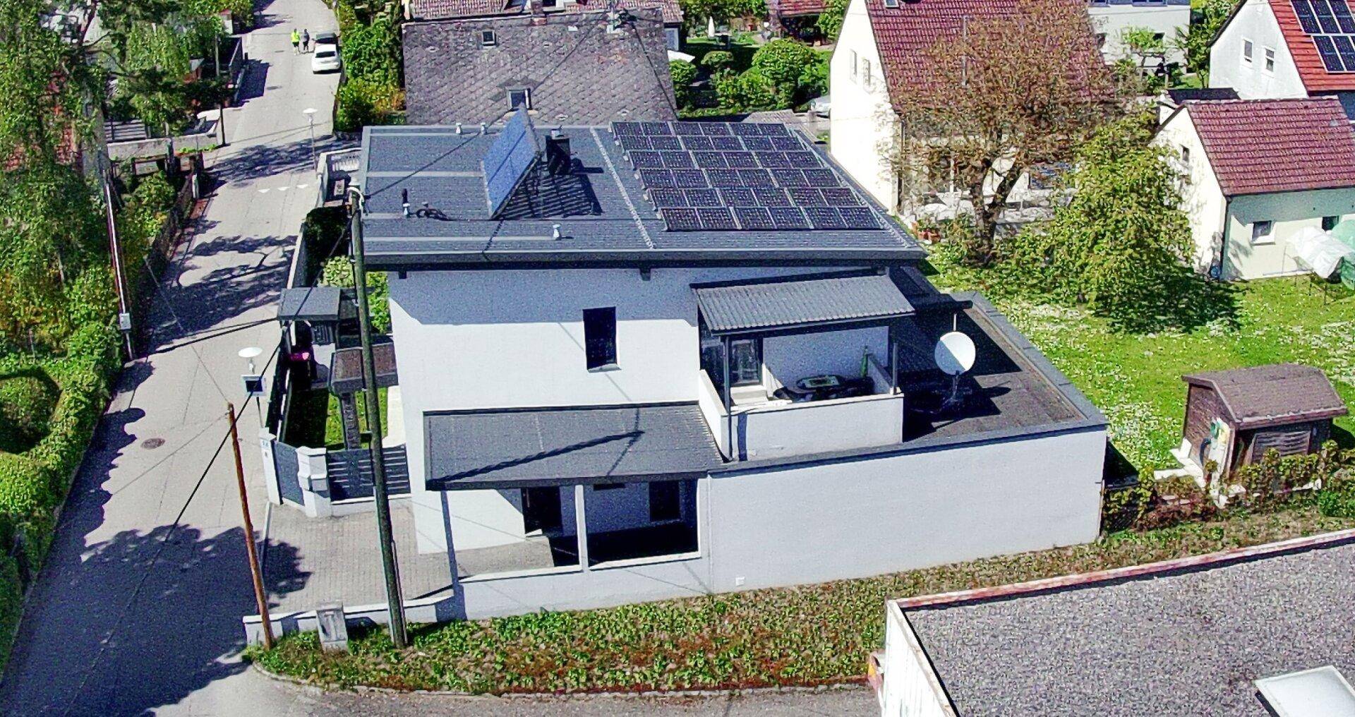 Luftaufnahme eines modernen Hauses mit Solaranlage und umliegender grüner Wohngegend.