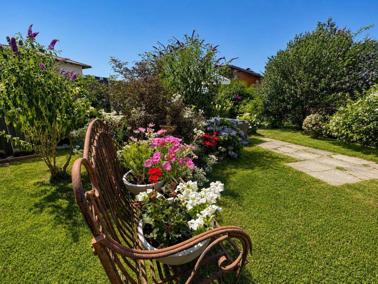 Idyllischer Gartenweg mit einer rustikalen Bank und farbenfrohen Blumenbeeten.