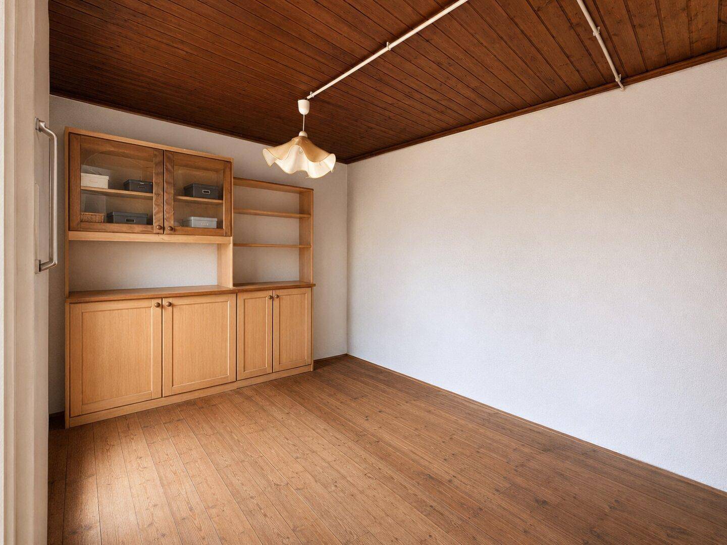 Leerer Raum mit Holzdielenboden und eingebautem Holzschrank, helle Wände.